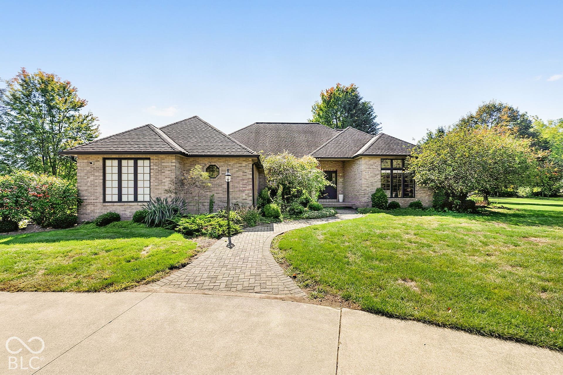 Brick exterior with dark-framed windows, a paver walkway, and mature landscaping