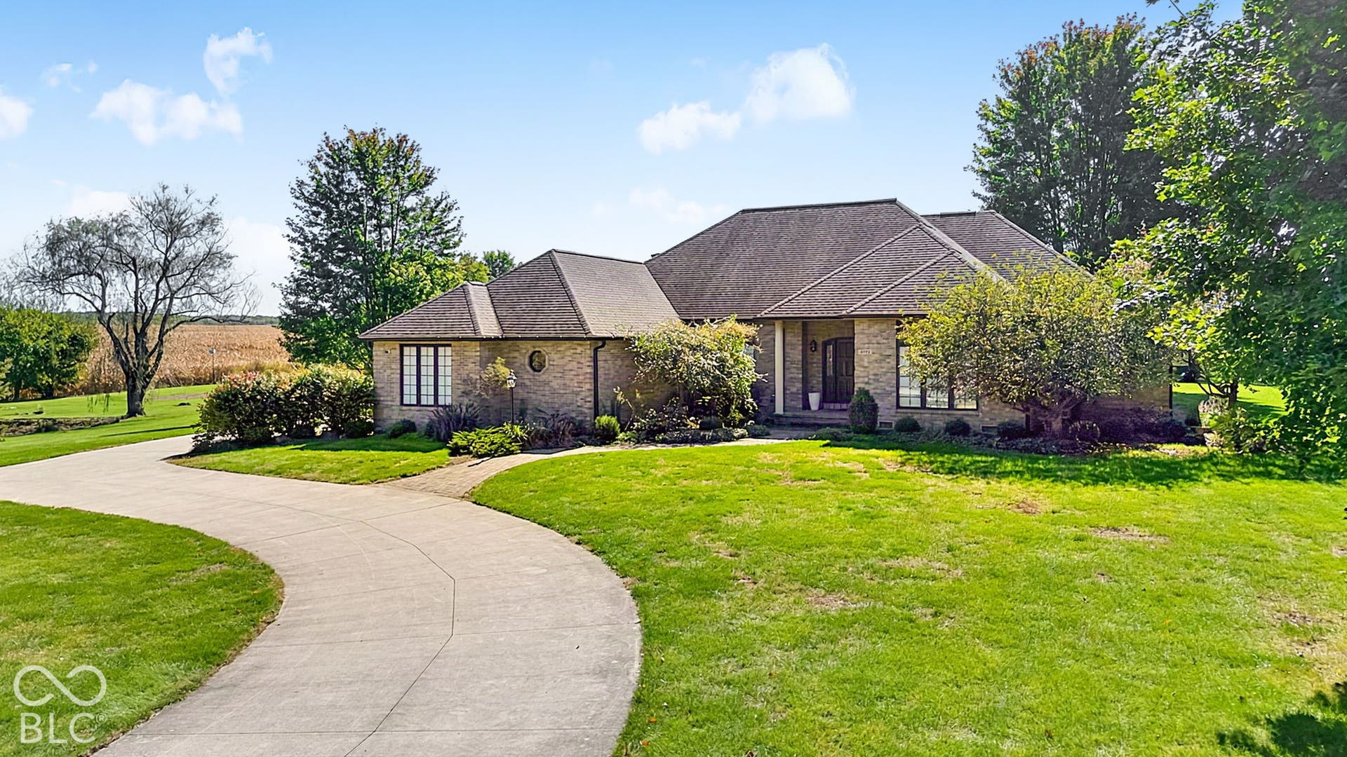 Brick exterior with a multi-pitch roof, expansive green lawn, mature trees, and a winding concrete driveway