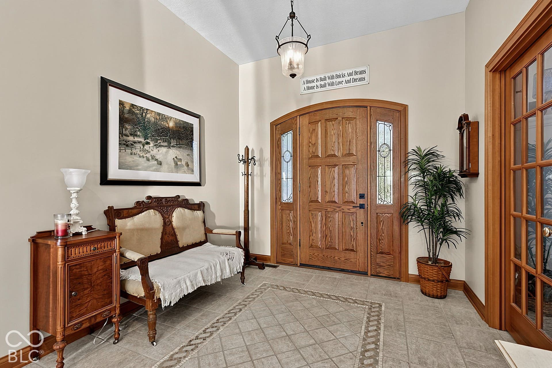 Arched solid wood entry door with decorative glass sidelights, tiled flooring with an inlaid pattern, and a grid-paneled interior door