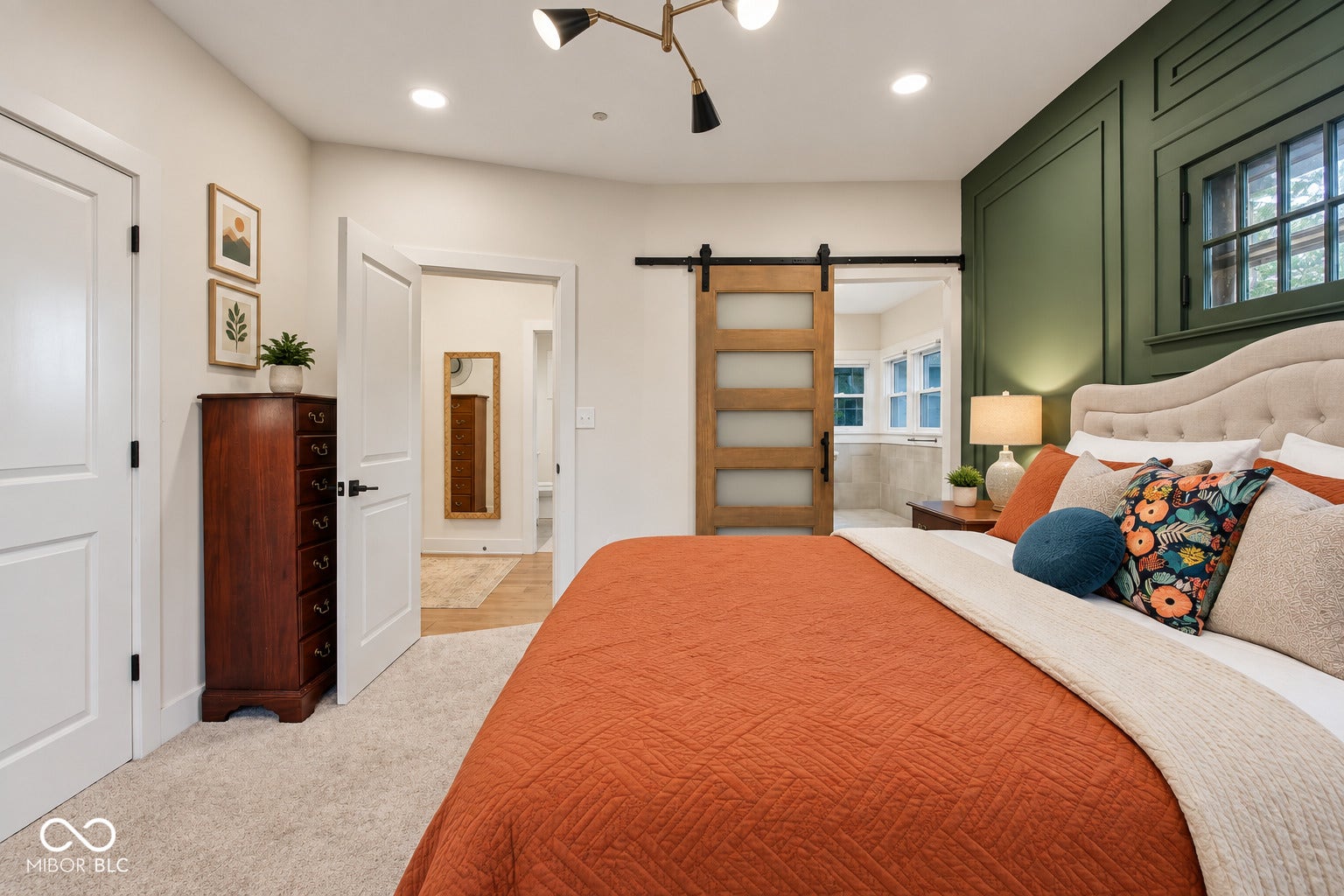 Tufted upholstered headboard, recessed lighting, wood-finish barn door with frosted panels, green accent wall with decorative trim, and a multi-directional ceiling light fixture
