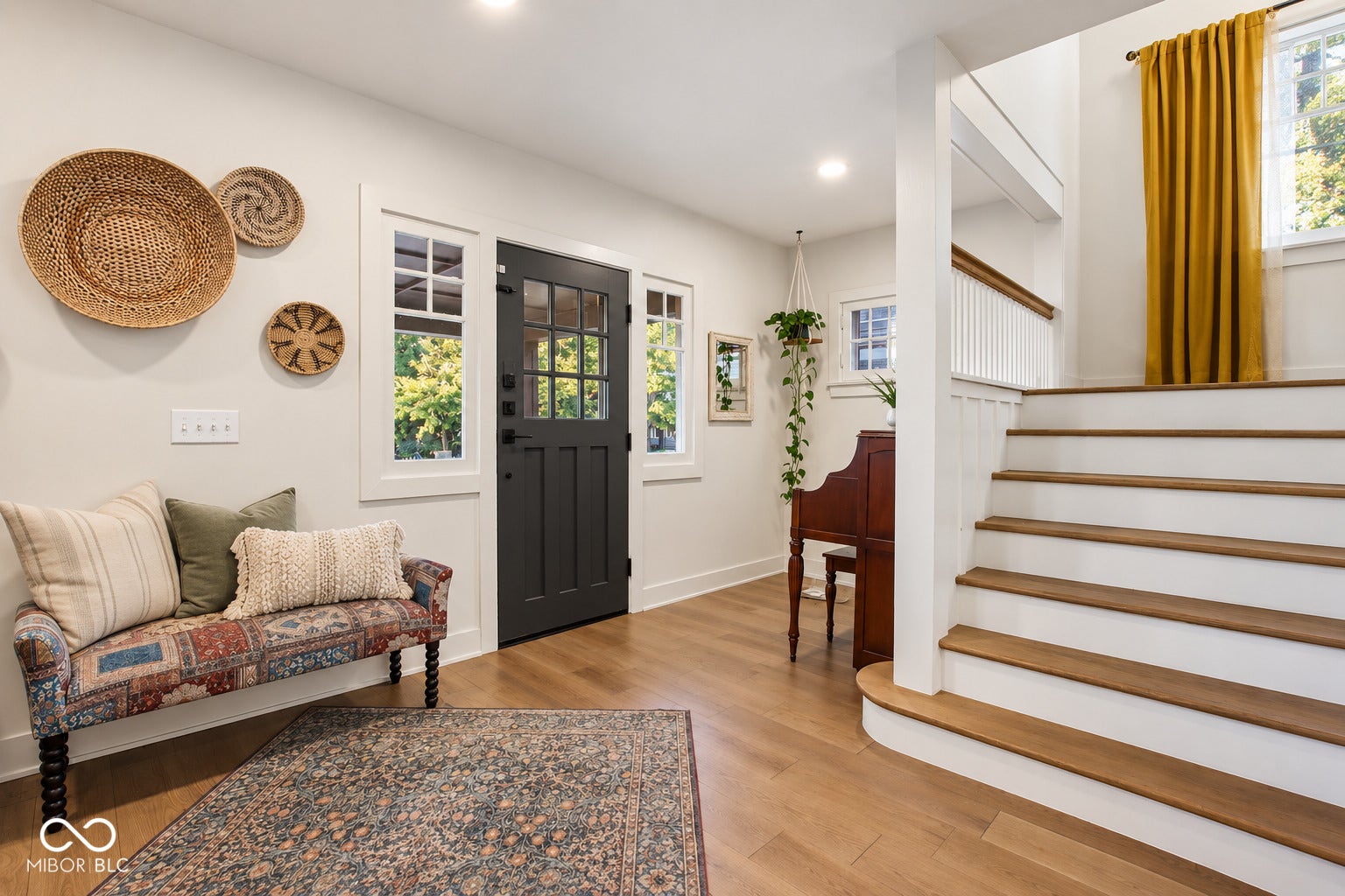 Hardwood flooring throughout the entry, a dark-paneled door with multiple windowpanes, and a well-lit staircase with natural wood treads