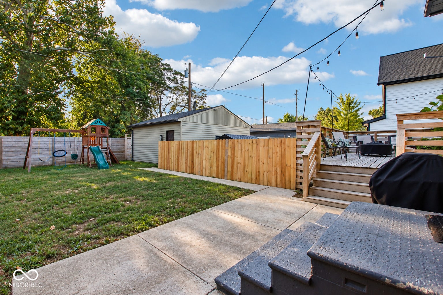 Spacious backyard featuring a wood deck, string lighting, concrete patio, and wood privacy fencing