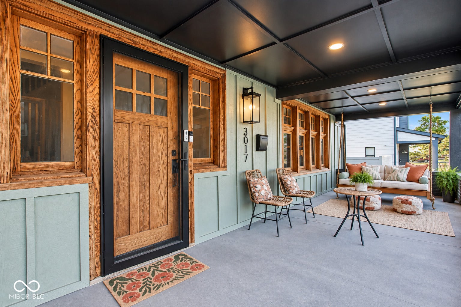 Covered front porch featuring a wood-panel entry door with transom windows, board and batten siding, recessed lighting, and a coffered ceiling