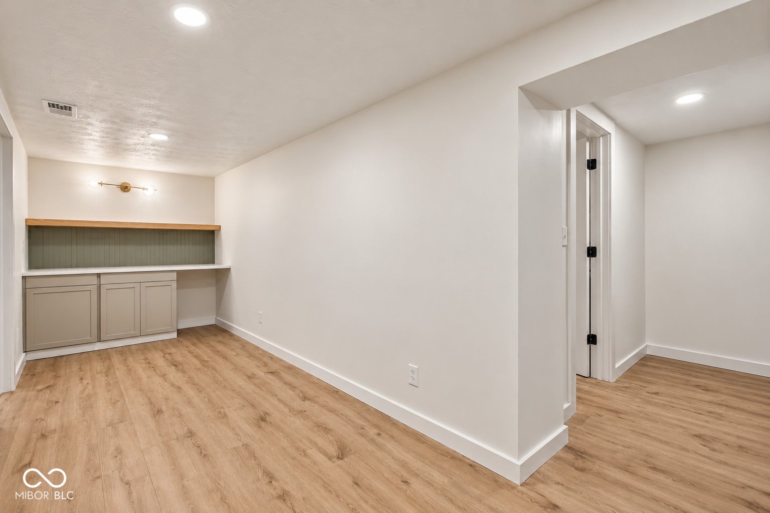 Virtually Altered - Wood-finish flooring throughout, built-in cabinetry with a light-toned countertop, and an accent wall featuring a sconce-style light fixture