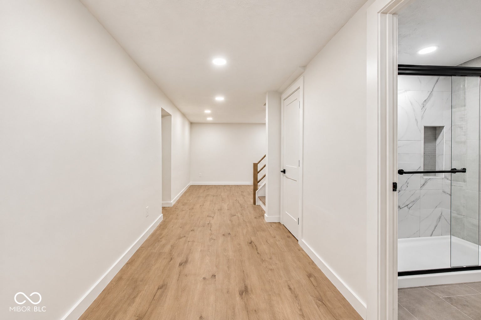 Virtually Altered - Spacious hallway with wood-finish flooring, recessed lighting, and a full bathroom featuring a glass-enclosed shower with tile surround and an integrated niche
