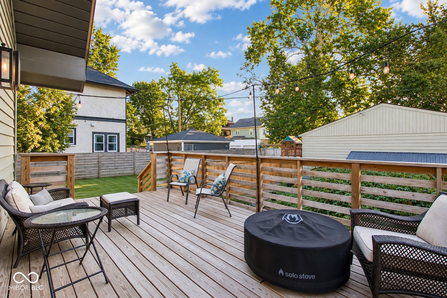 Expansive wood deck with a slatted wood railing, featuring string lighting and an exterior wall lantern