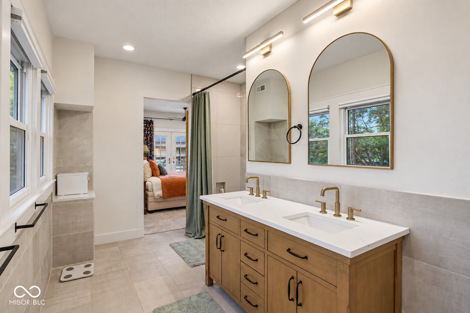Dual arched mirrors, dual vanity with wood-finish cabinetry, white countertop, and gold-finish fixtures