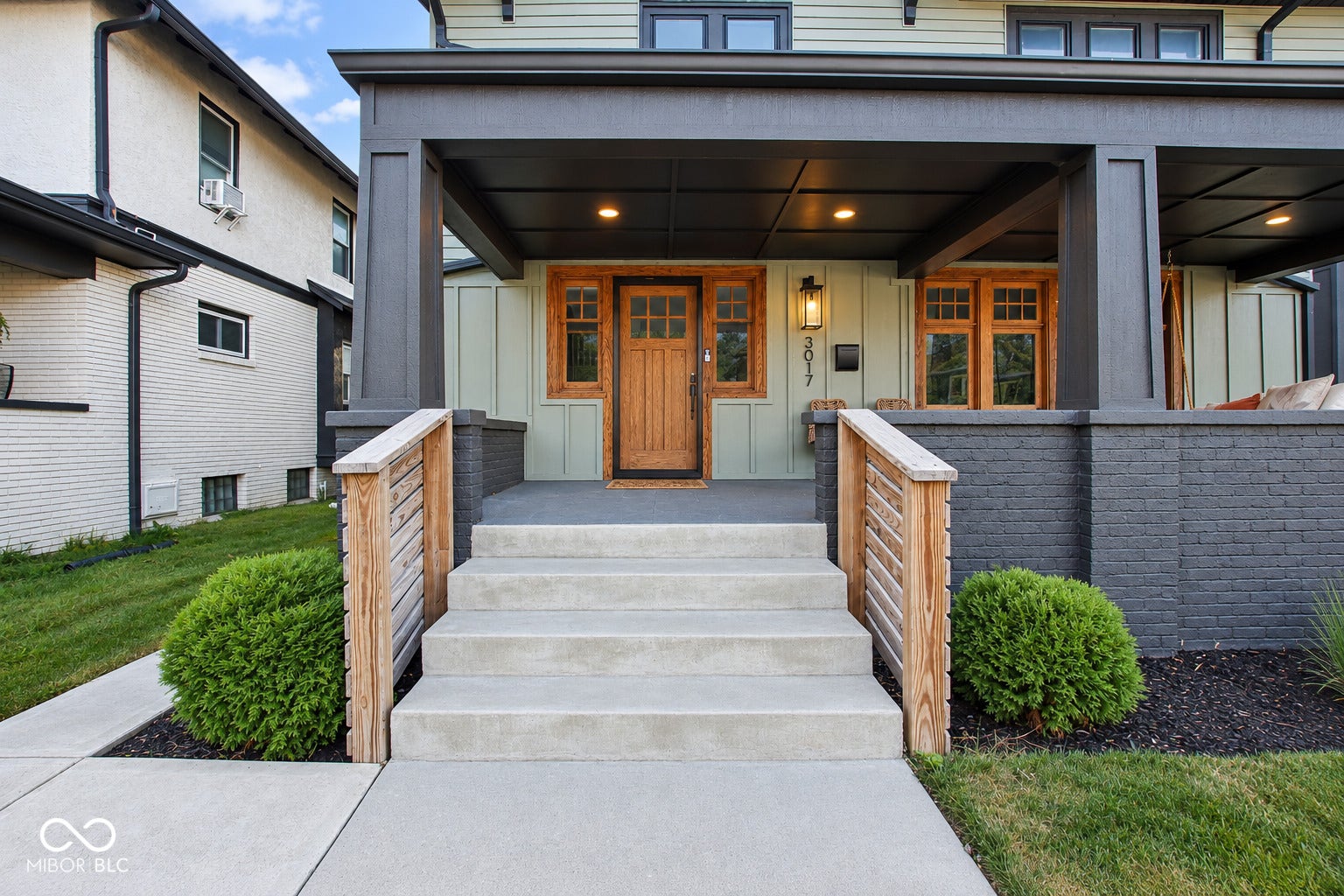 Covered porch entry featuring wood-finish door, sconce lighting, and painted brick accents