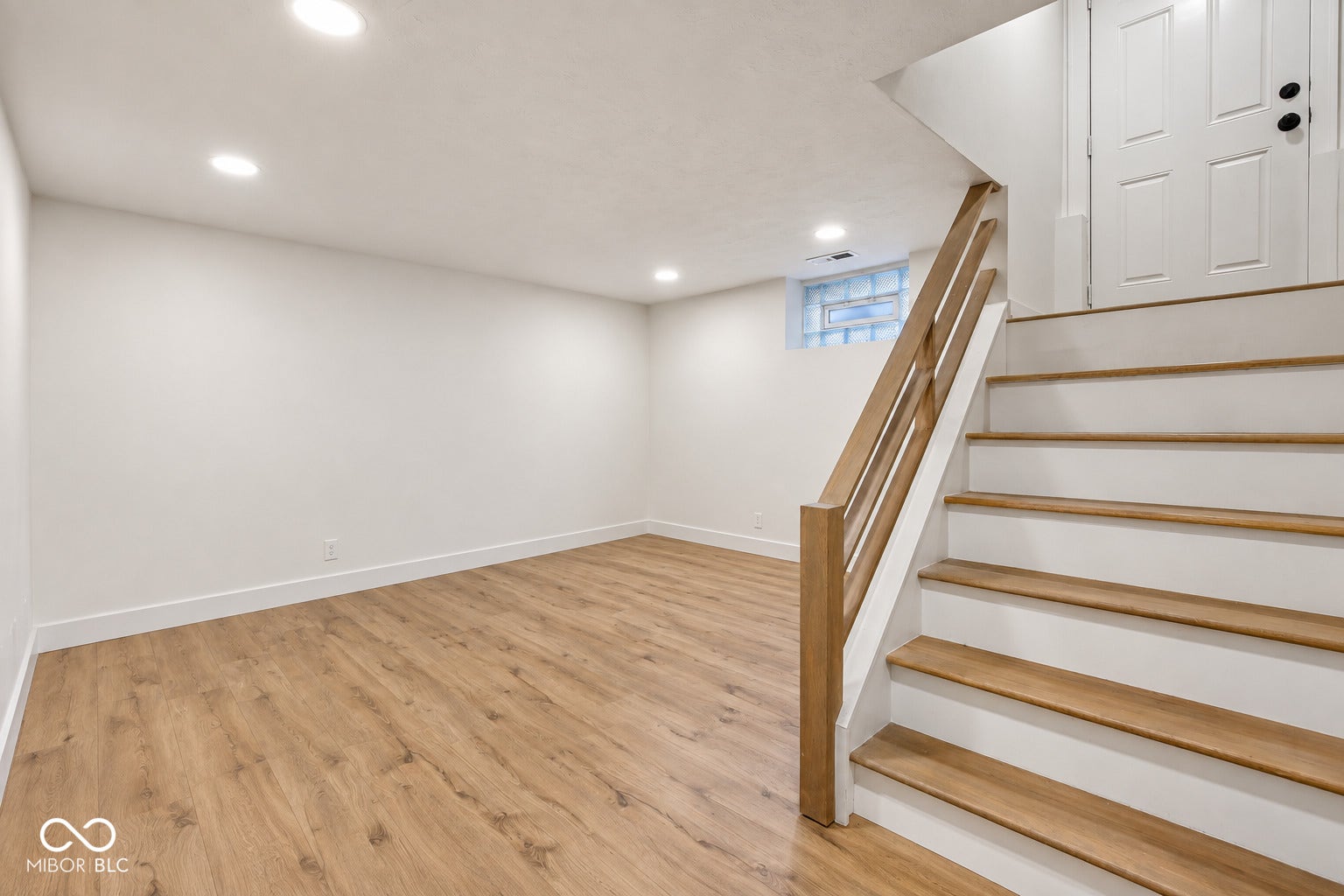 Virtually Altered - Recessed lighting illuminates the open area, featuring wood-finish flooring and a wood-finish staircase with white risers