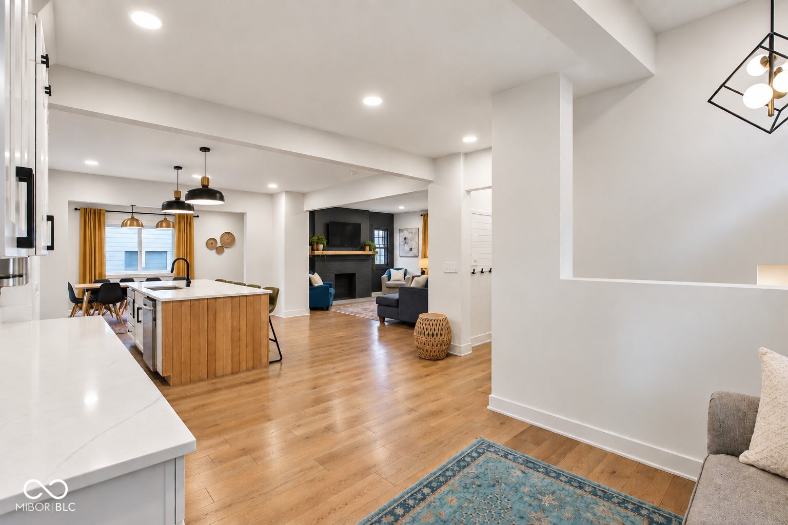 Open-concept living area with wood-finish flooring, a kitchen island with a built-in sink, recessed lighting, and a dining area with pendant lighting