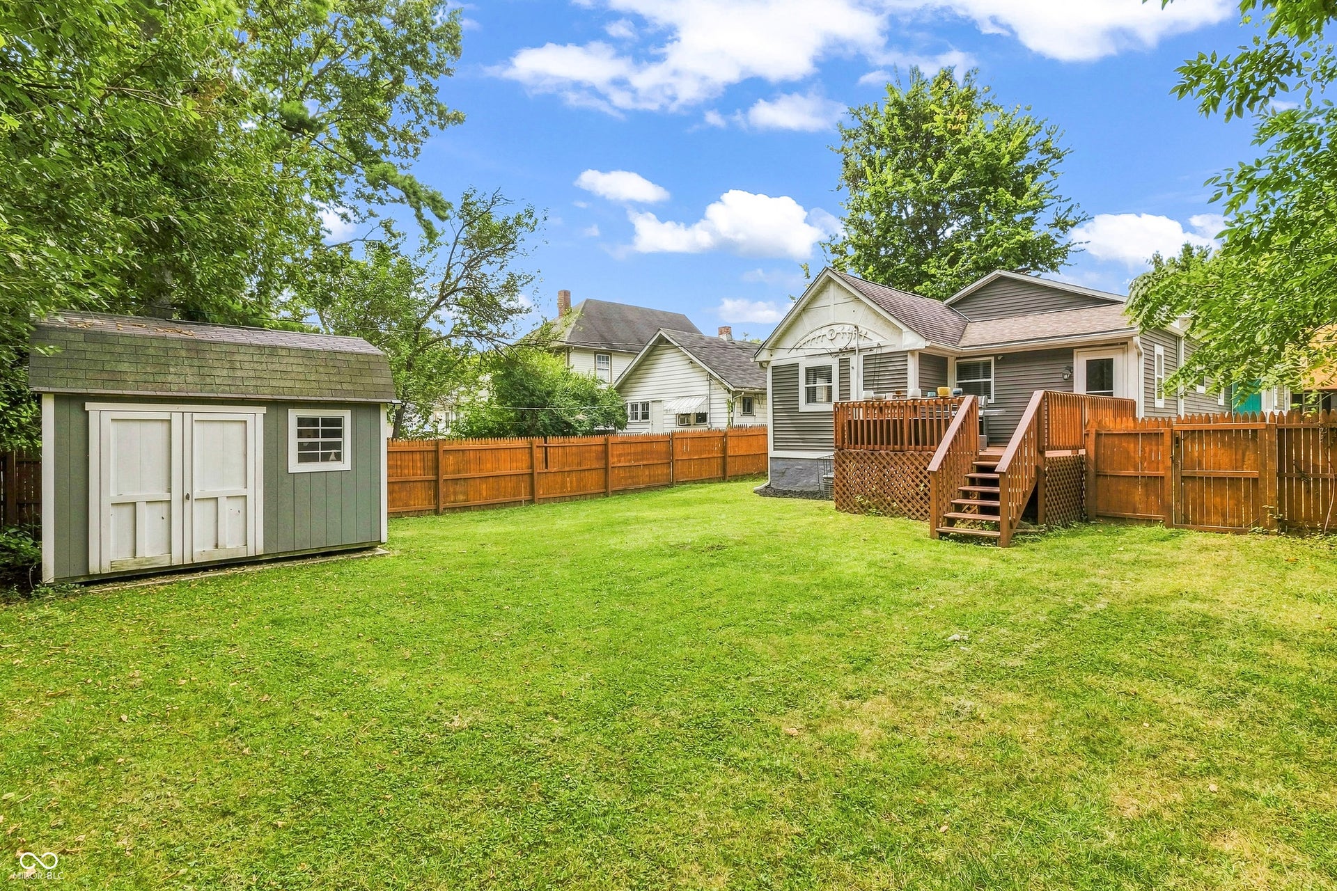 Expansive backyard with a manicured lawn, full wood privacy fencing, a wood deck with stairs, and spacious detached storage shed