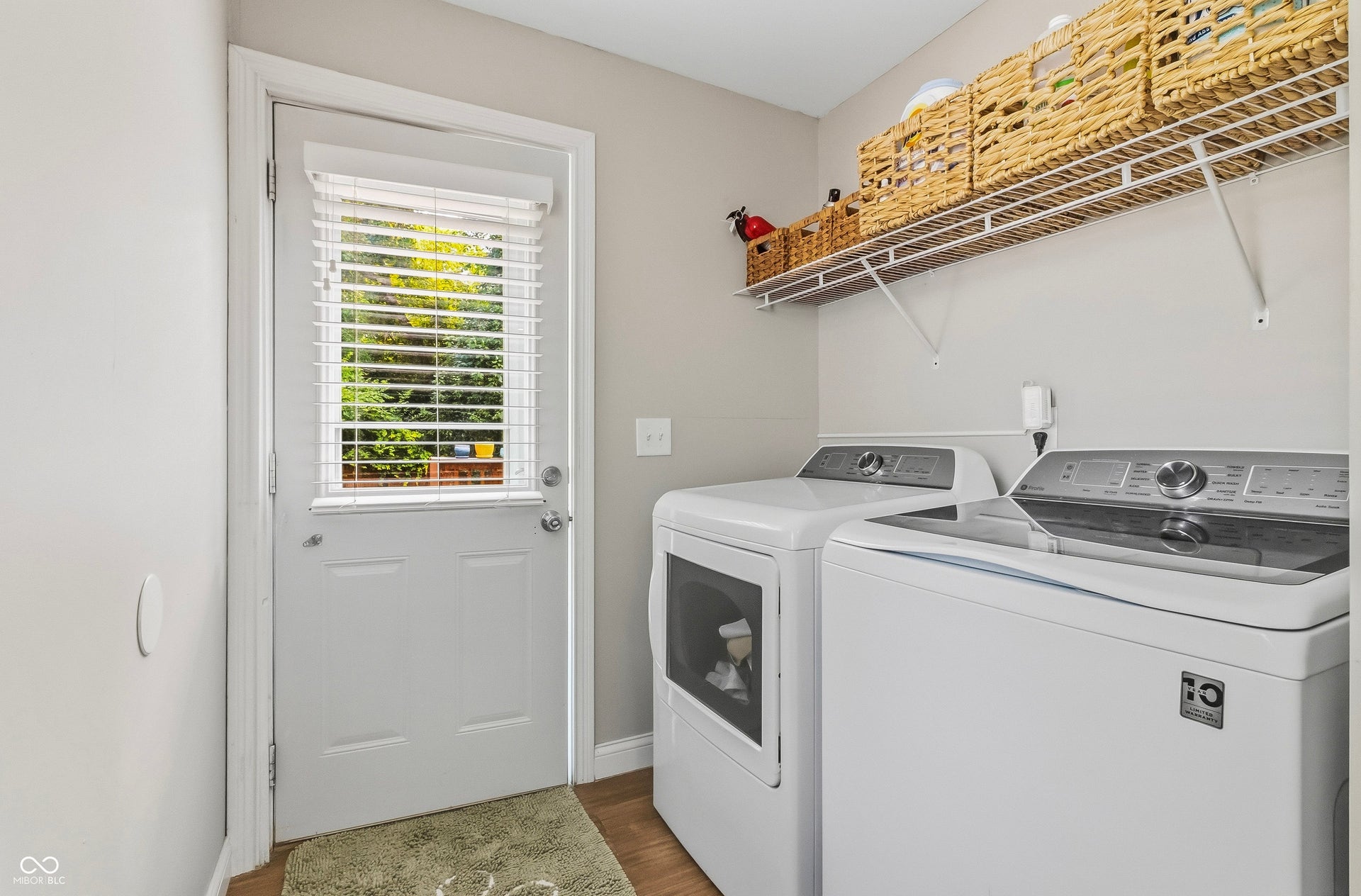 Laundry area next to rear door entry way featuring wire shelving unit for storage. Washer and Dryer stay.
