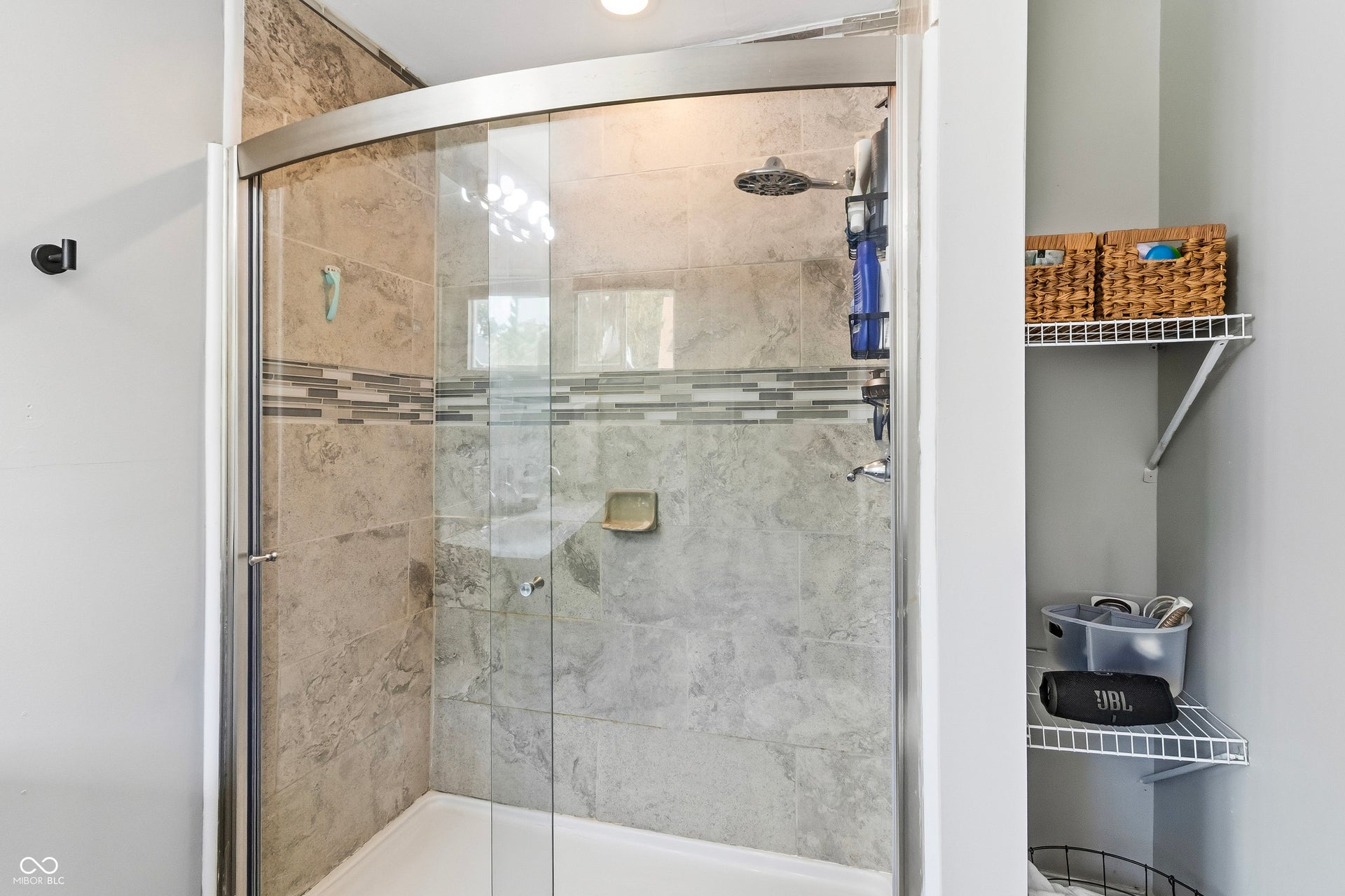 Shower enclosure with glass sliding doors, tiled walls, decorative accent tile band, built-in shower head, and shelving for extra storage.