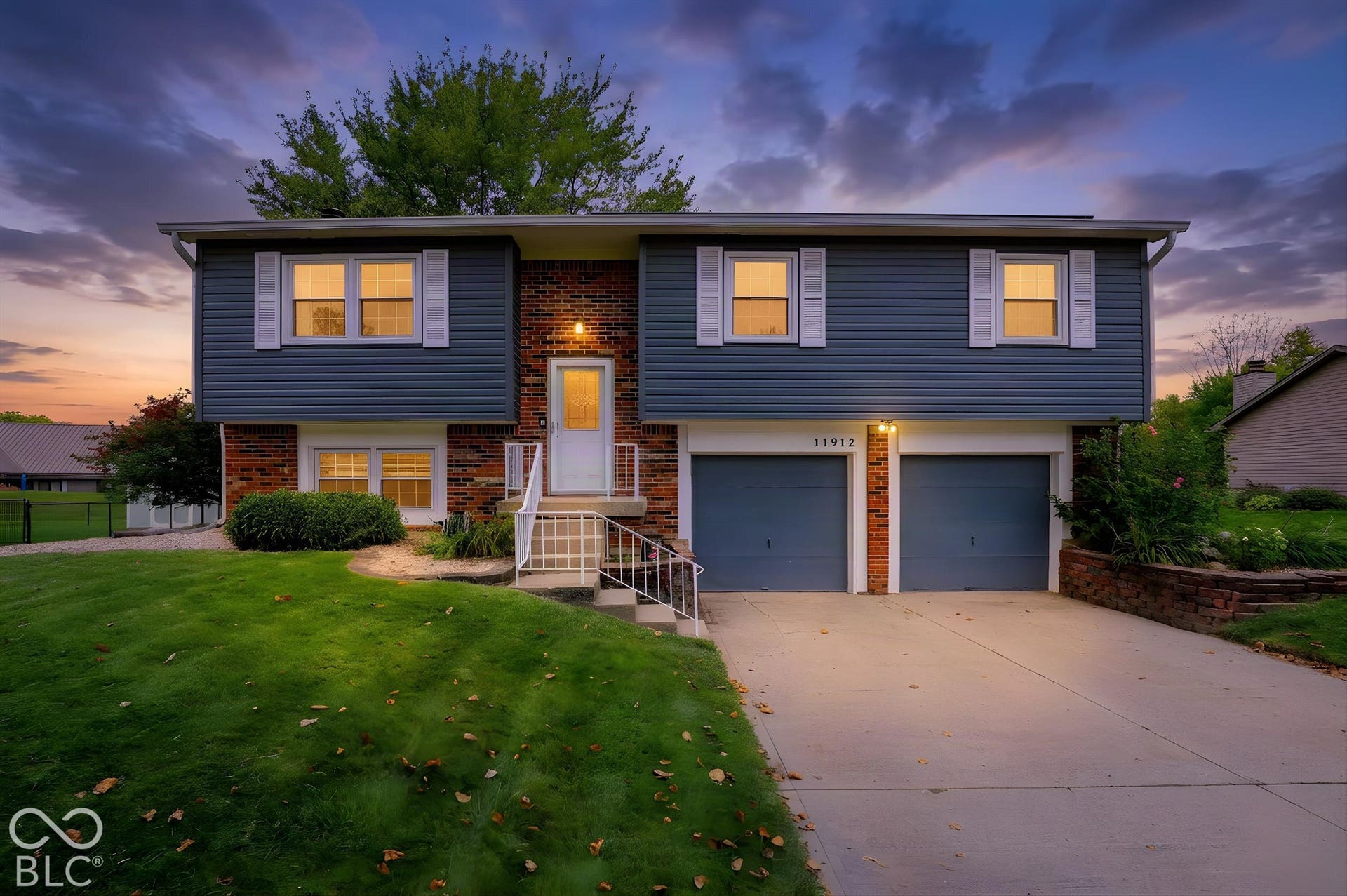 Virtually Altered - Split-level exterior featuring horizontal siding, brick masonry detailing, an attached two-car garage, and white louvered window shutters