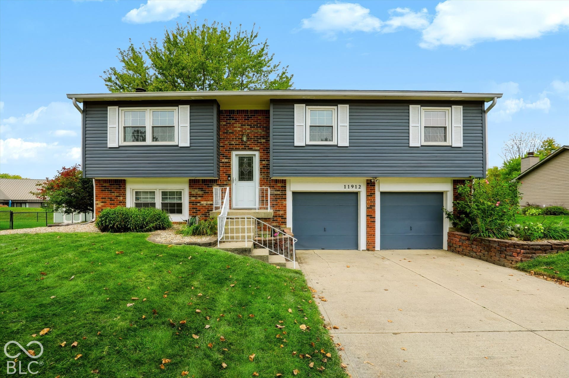 Split-level exterior featuring dark blue horizontal siding, red brick accents, two-car garage with overhead doors, and concrete driveway