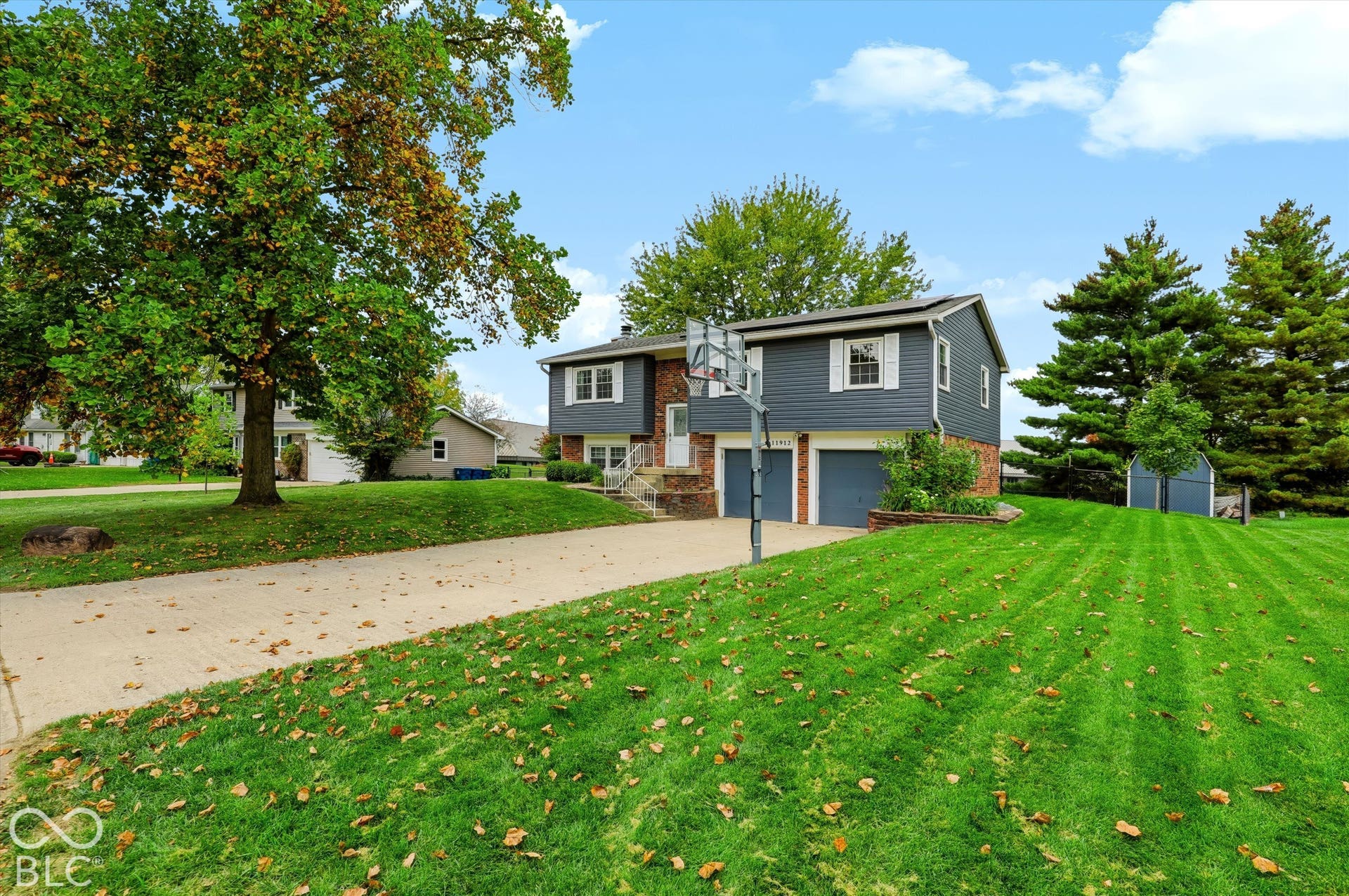 Split-level exterior featuring dark horizontal siding, a stone facade element, a two-car garage, and expansive lawn with mature trees