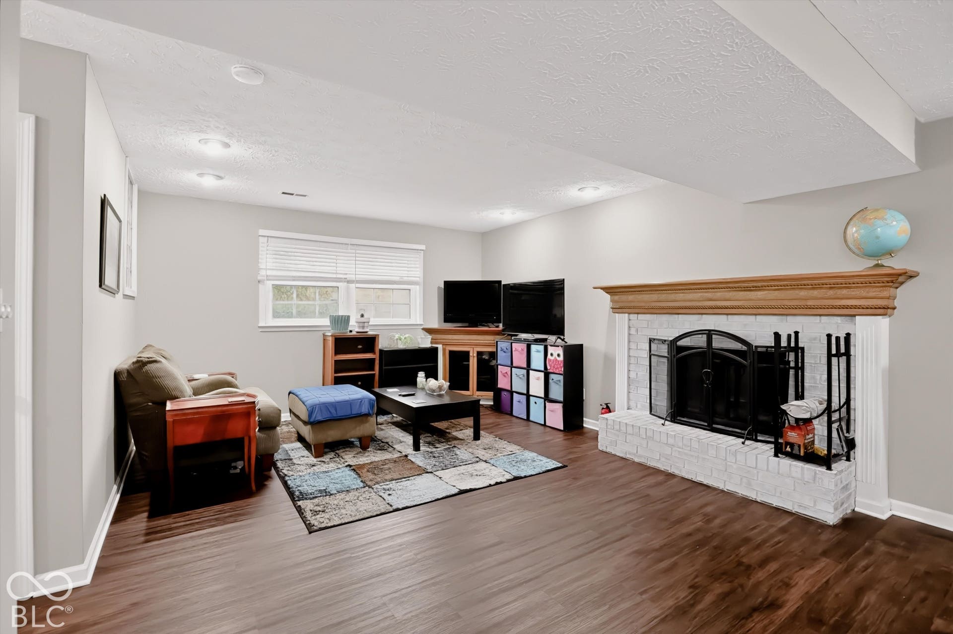Painted brick fireplace with a wood mantel, recessed lighting, and wood-finish flooring