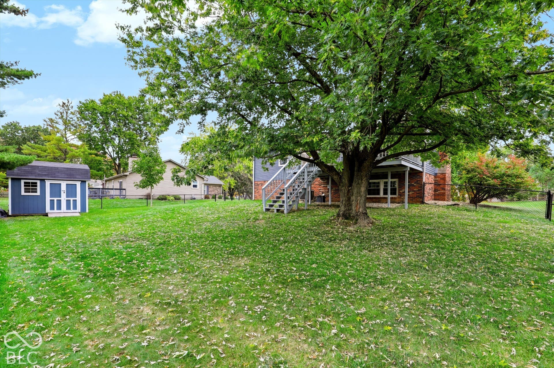 Expansive backyard featuring mature tree canopy, detached storage shed, exterior staircase, and perimeter fencing