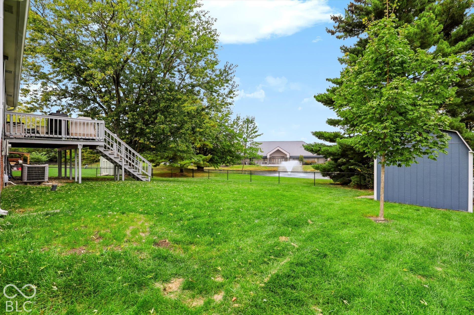 Backyard featuring a raised wooden deck with stairs, a detached storage shed, a fenced perimeter, and established trees