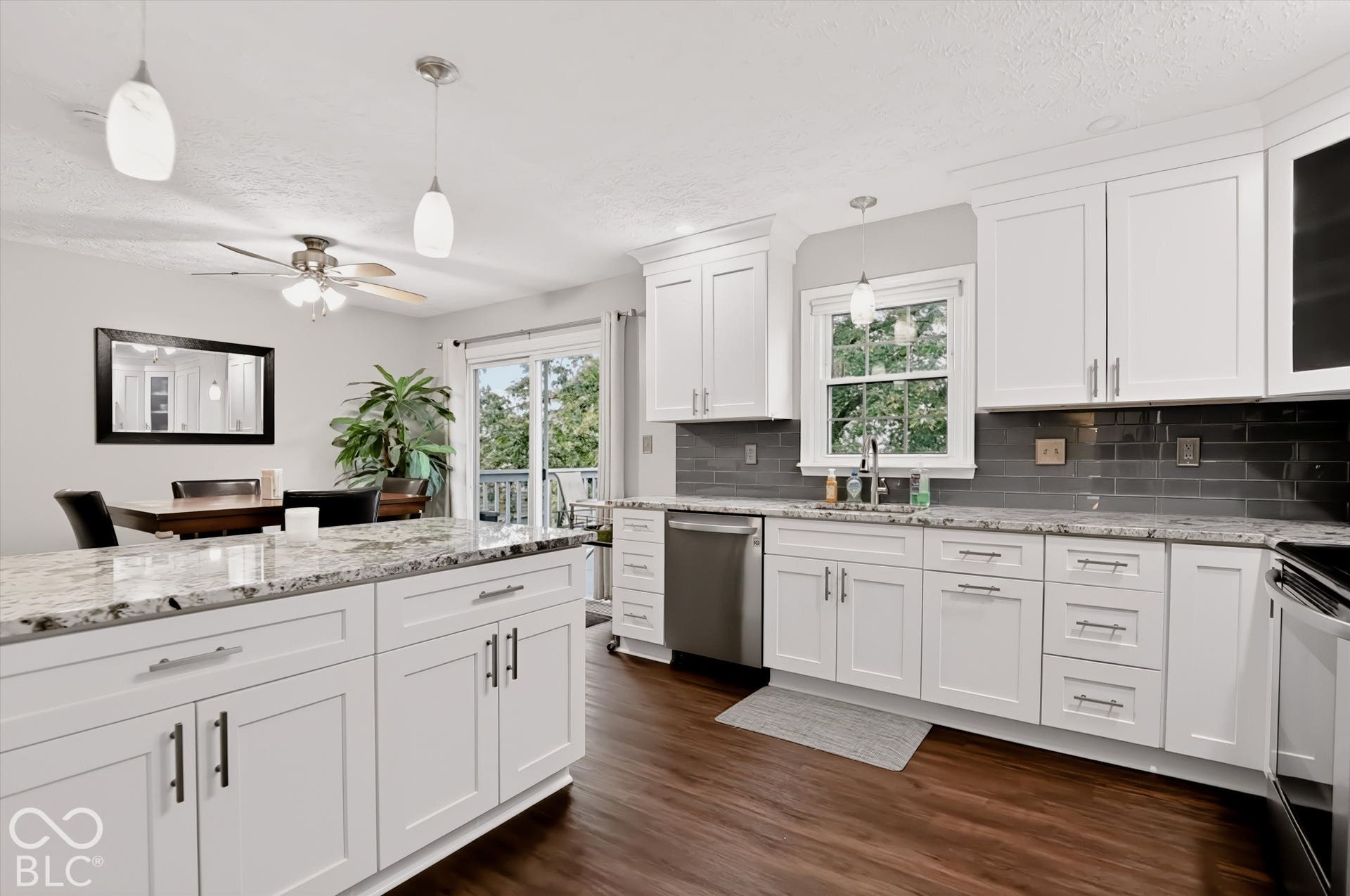 Kitchen featuring white shaker-style cabinetry, stone-patterned countertops, dark subway-style tile backsplash, stainless steel appliances, and wood-finish flooring