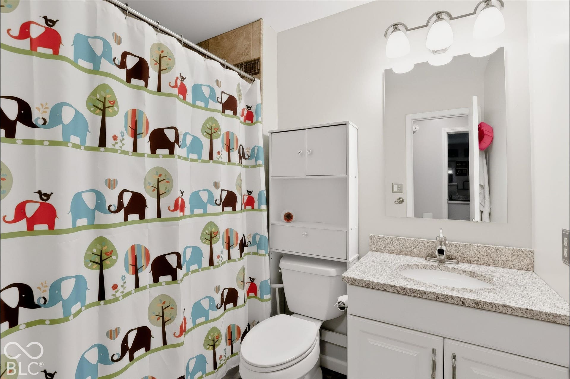 Bathroom featuring a vanity with a stone-finish countertop, undermount sink, three-light fixture, and wall-mounted mirror