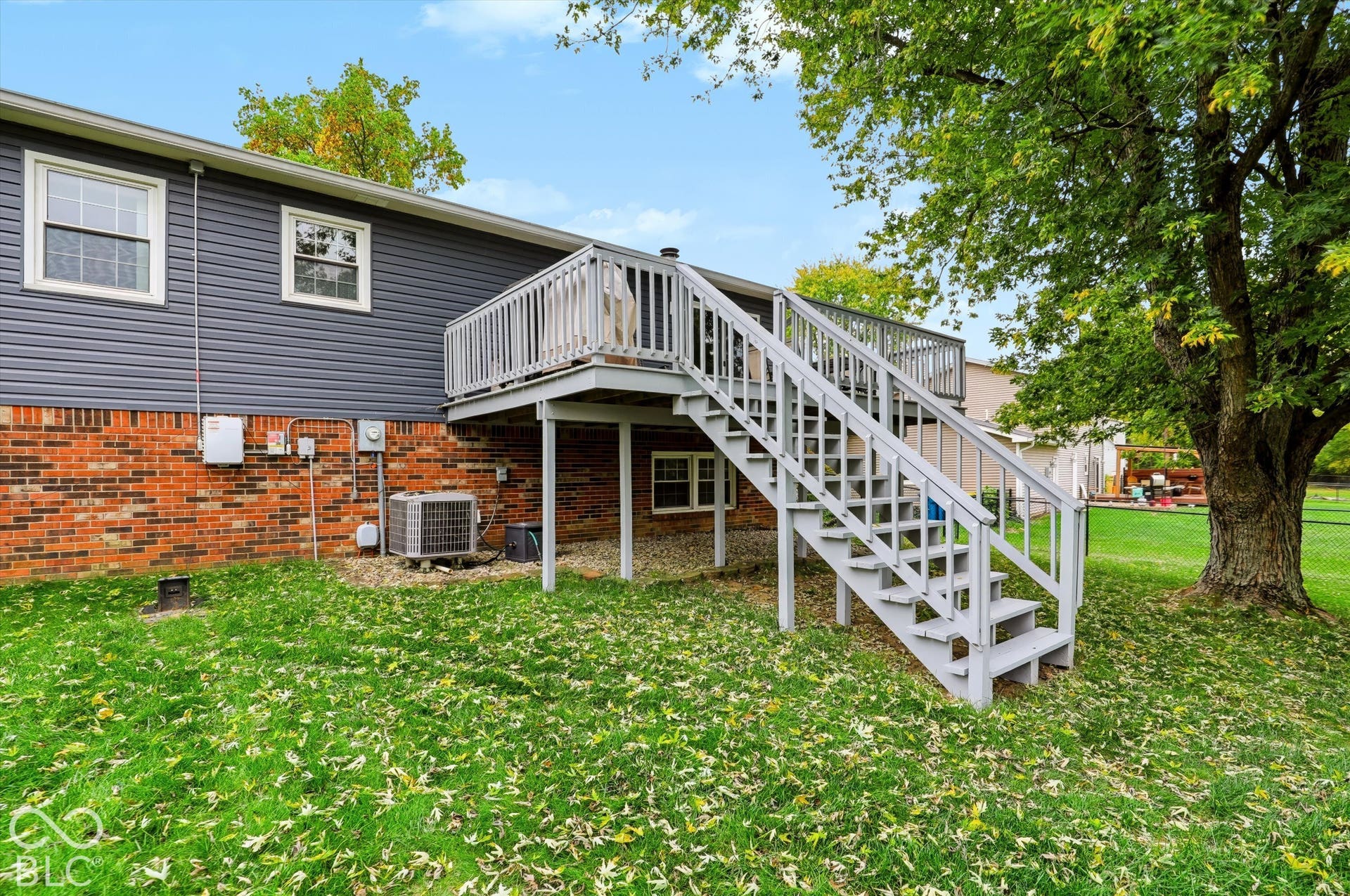 Elevated wooden deck featuring a staircase, horizontal siding, brick masonry, and mature trees