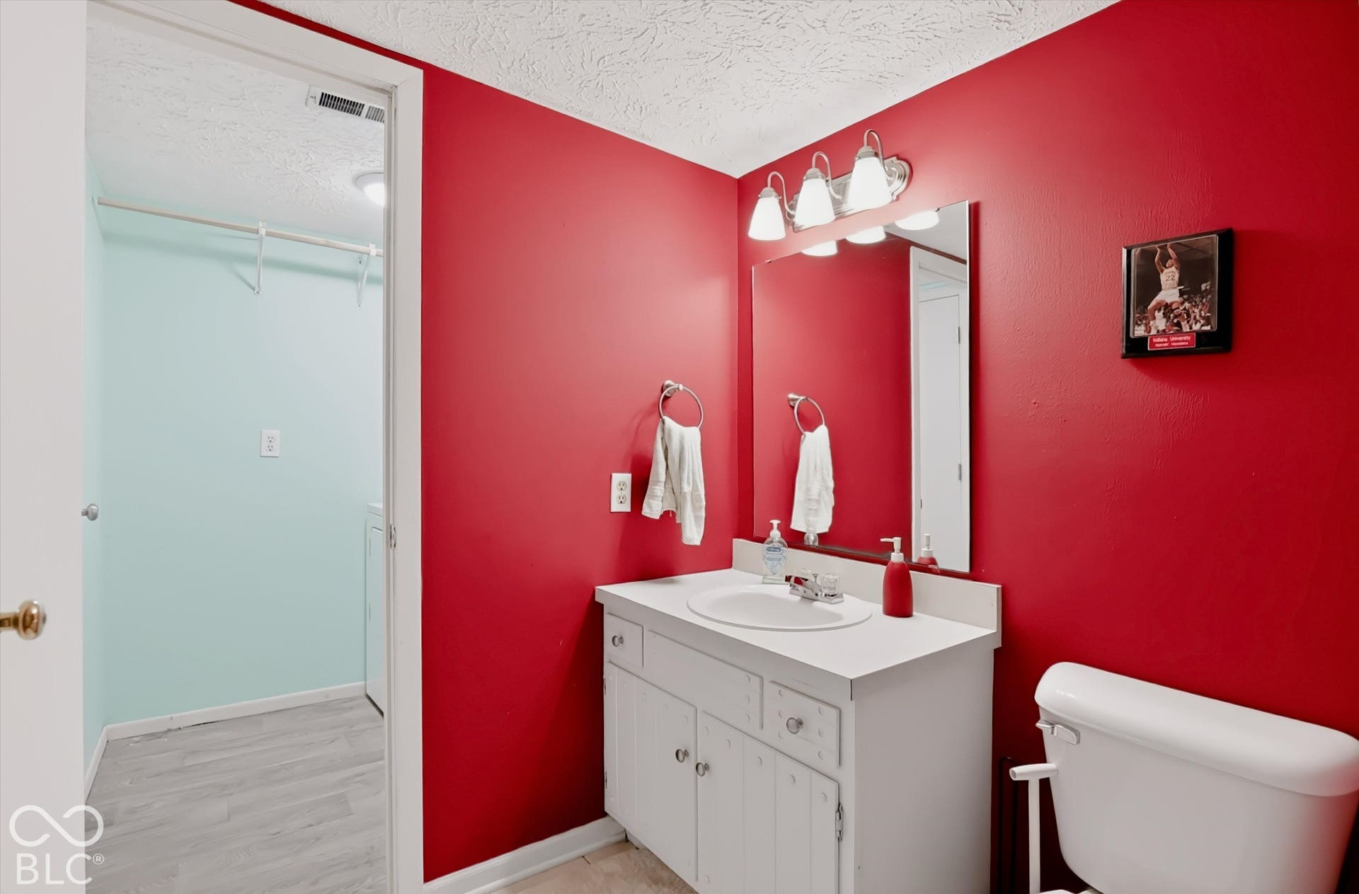 Bathroom featuring a white vanity cabinet with a round integrated sink, a rectangular wall-mounted mirror, a three-light fixture, and a standard toilet