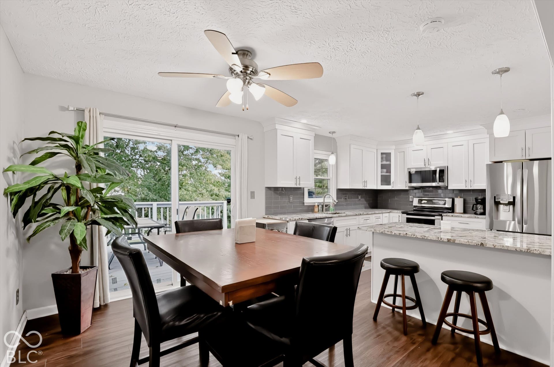 Kitchen featuring white cabinetry, stone-surface countertops, subway tile backsplash, stainless steel appliances, and wood-finish flooring