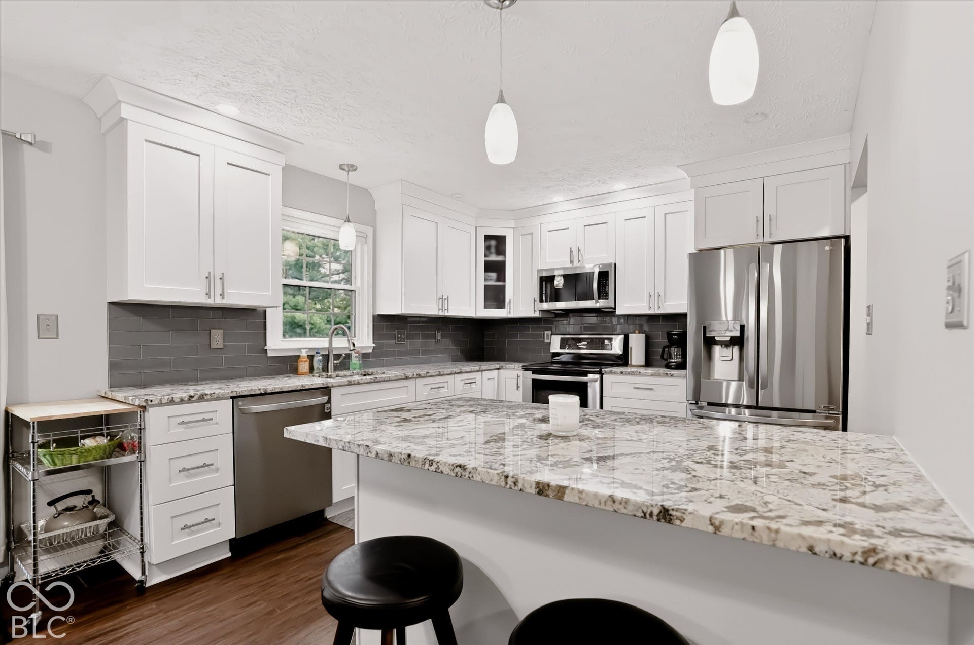 Kitchen featuring white cabinetry, stone countertops, dark-toned tile backsplash, stainless steel appliances, and wood-finish flooring