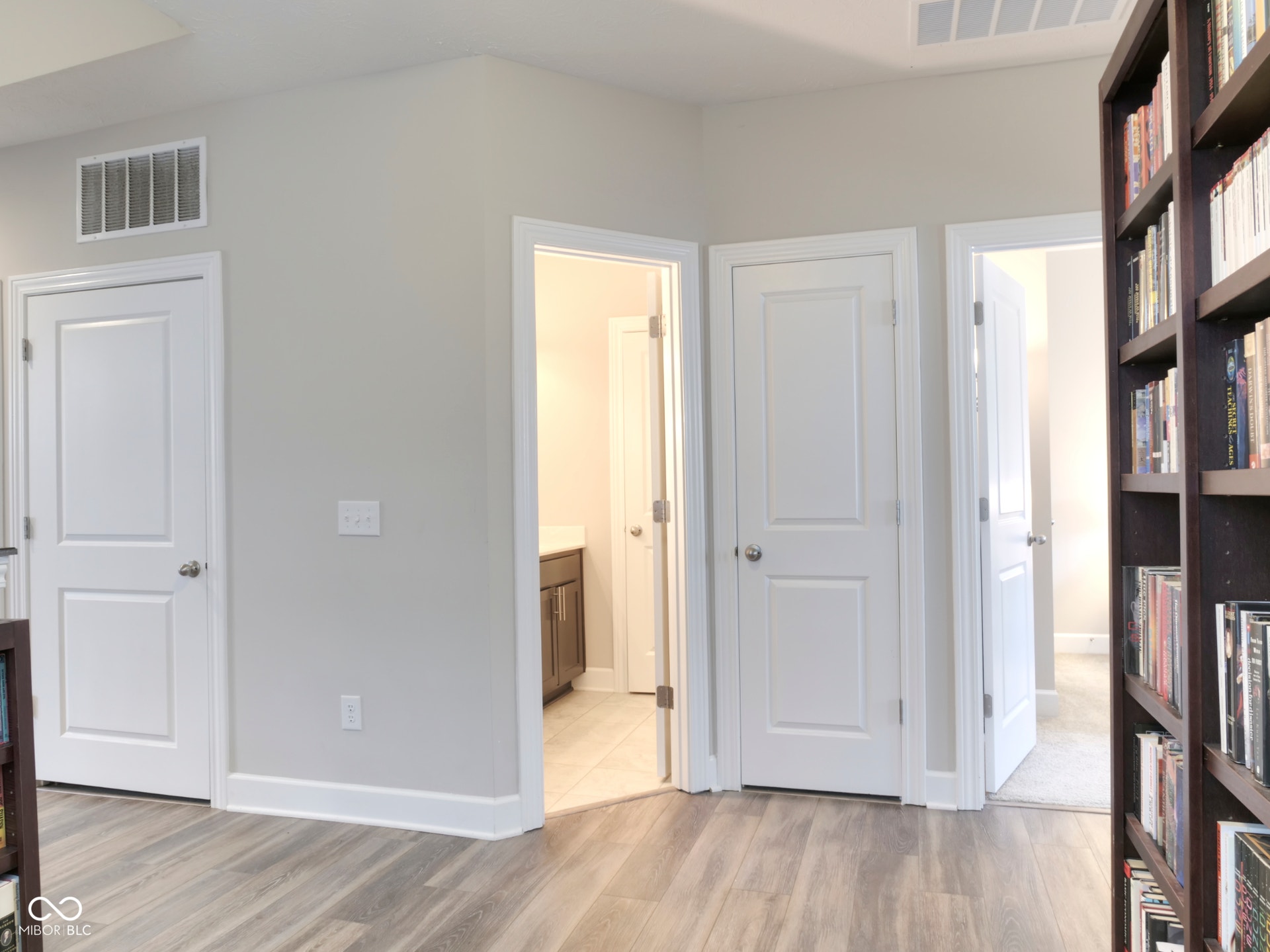 Wood-finish flooring, white paneled doors, light gray wall paint, and white trim