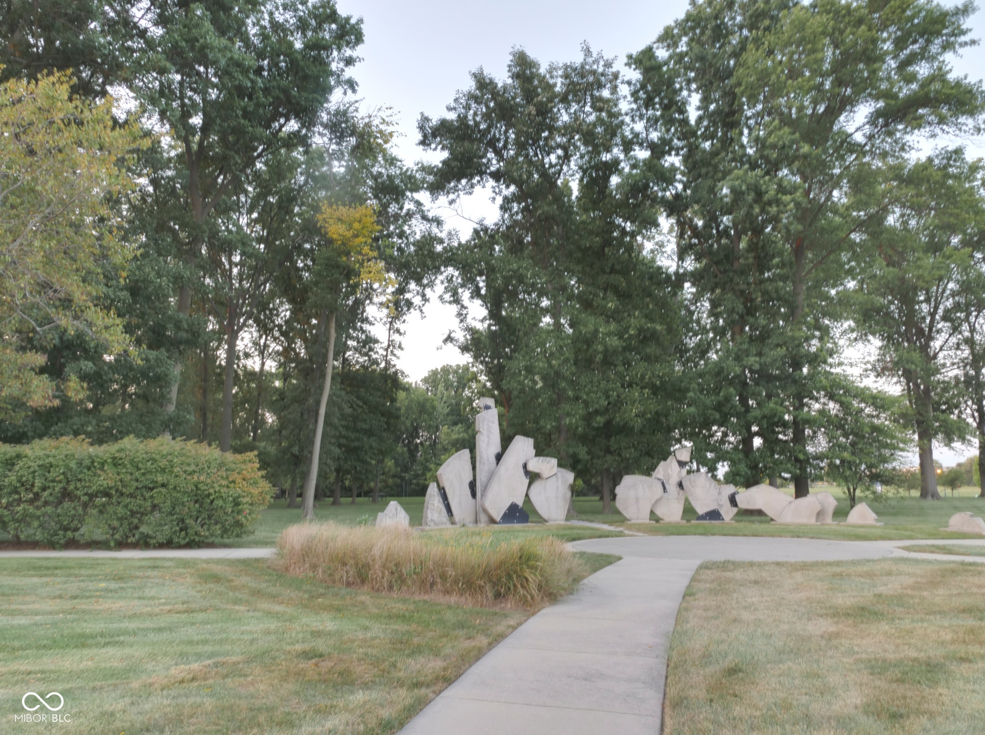 Expansive grounds featuring a meandering pathway, mature trees, and sculptural stone elements