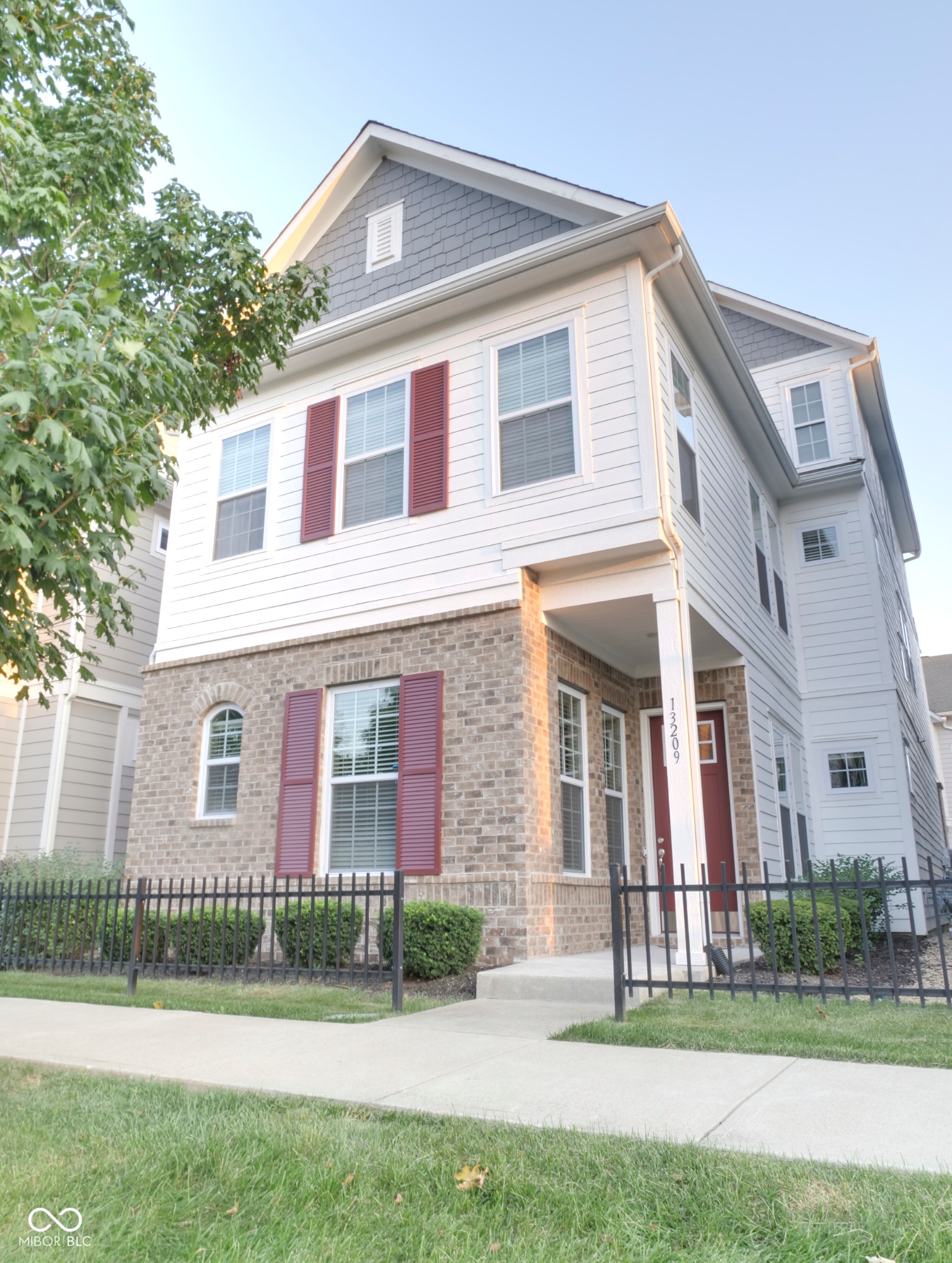 Three-story facade with brick and horizontal siding, red window shutters, and a covered porch entry