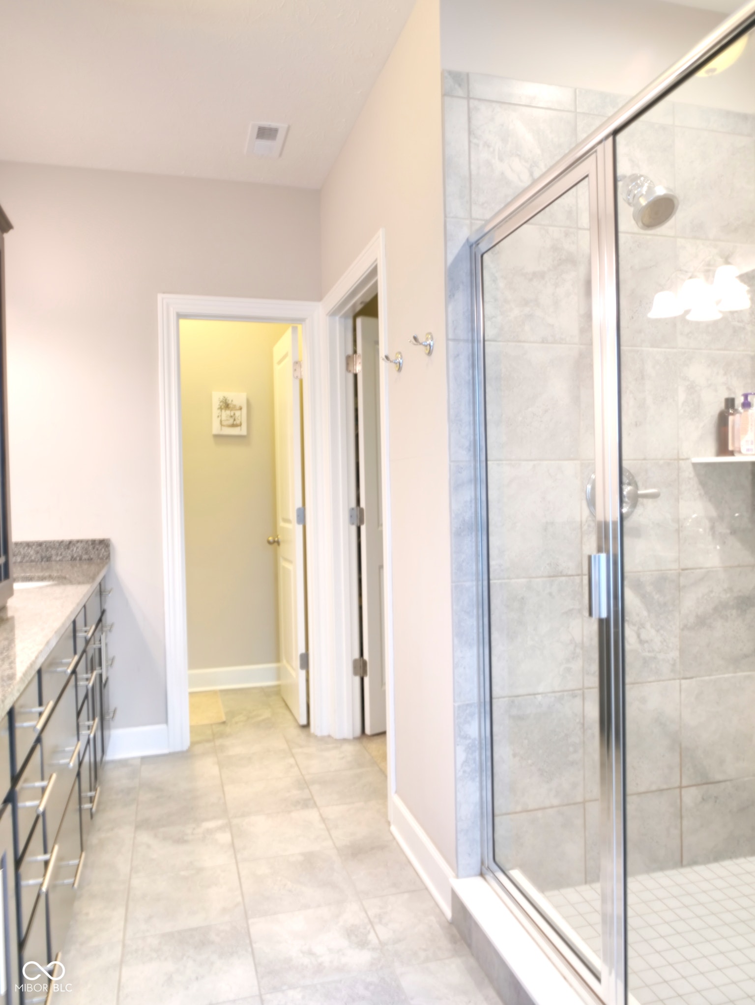 Tile flooring, built-in vanity with granite countertop, chrome hardware, glass-enclosed shower, and tile shower surround