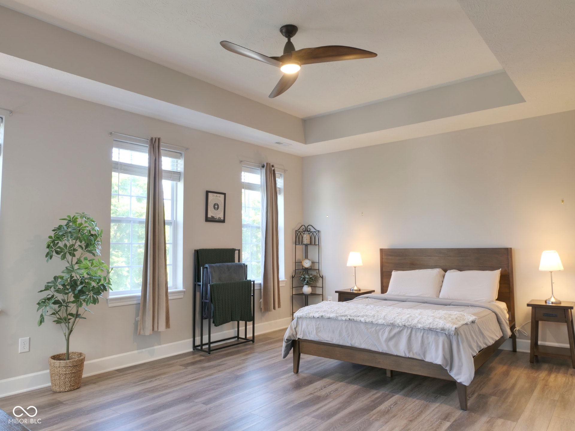 Tray ceiling with a ceiling fan, wood-finish flooring, and multiple windows