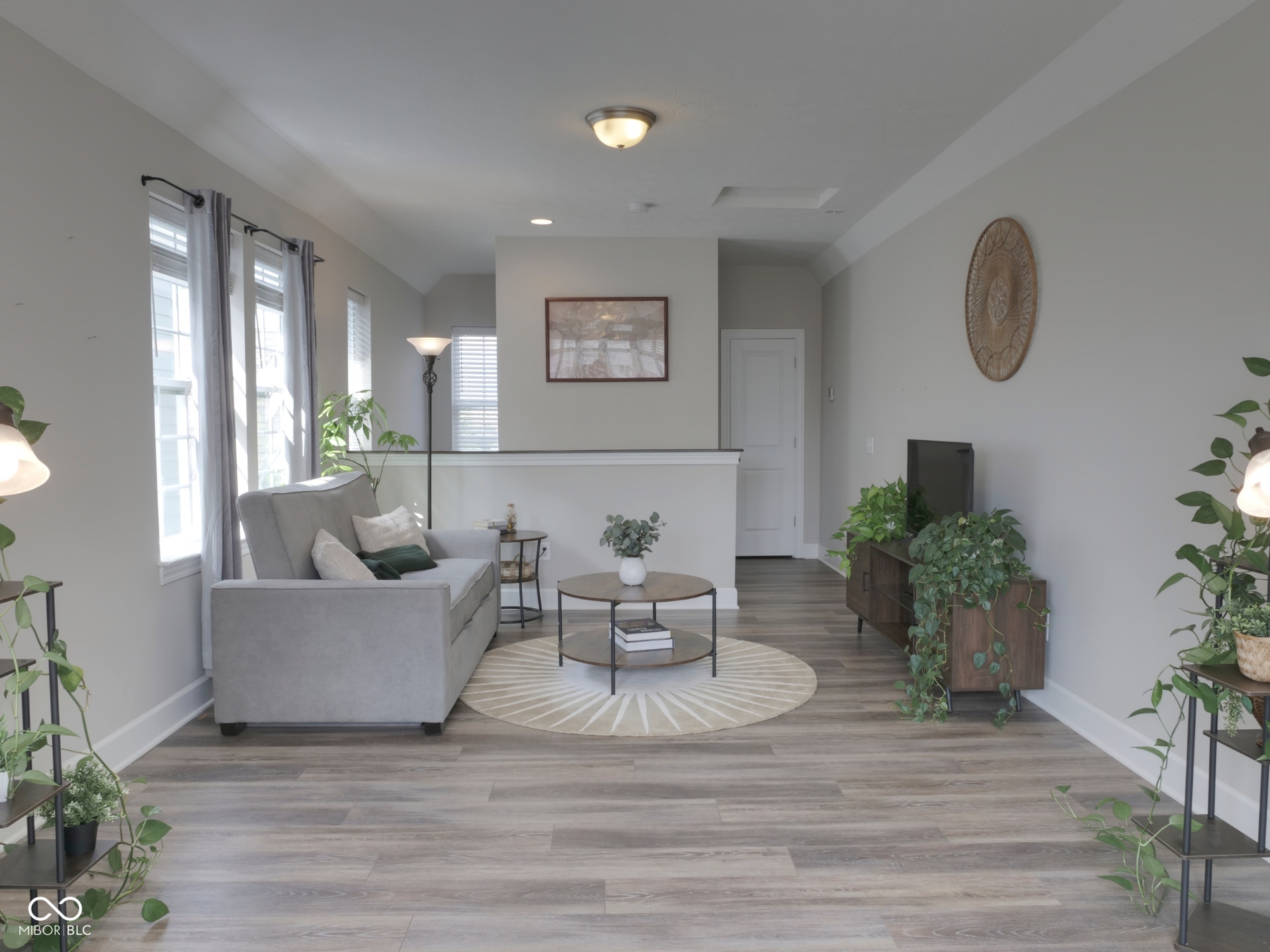 Wood-finish flooring, multiple windows providing natural illumination, ceiling-mounted light fixtures, and white trim work