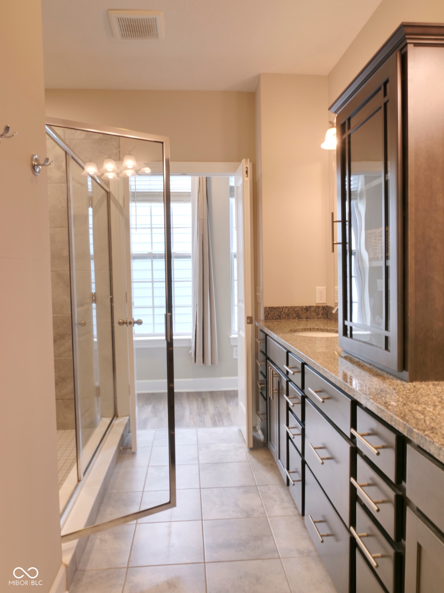 Spacious bathroom featuring a glass-enclosed shower, dual vanity with granite countertop, extensive cabinet storage, and tile flooring