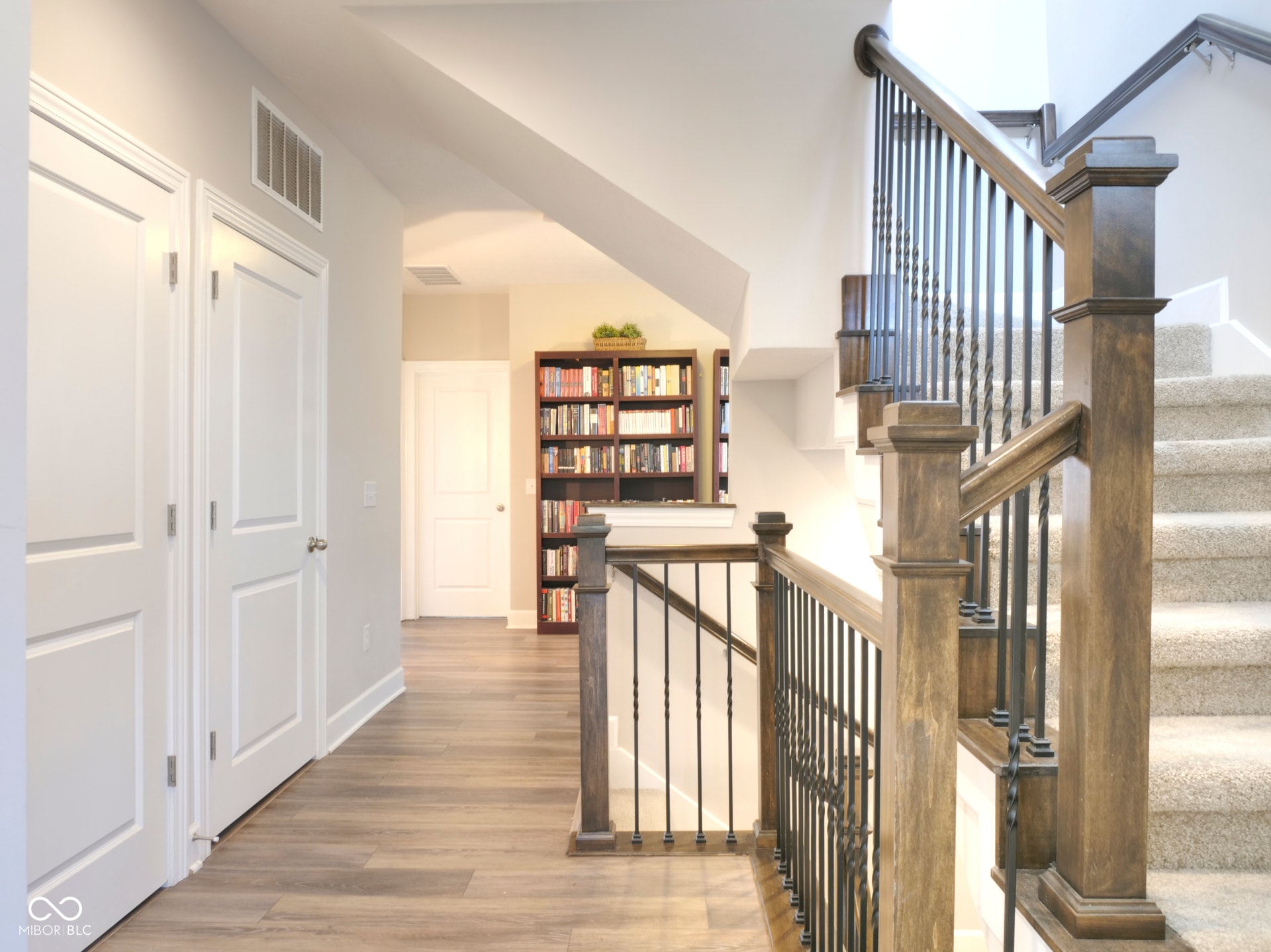 Wood-finish flooring with a staircase featuring dark wood newel posts, railings, and wrought iron balusters
