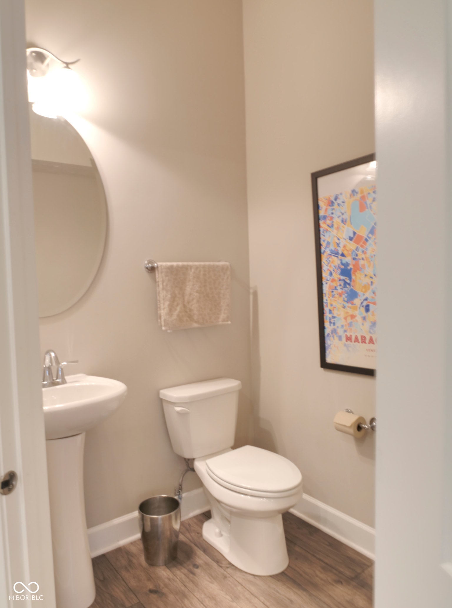 Pedestal sink with chrome faucet, round wall mirror, white toilet, and wood-finish flooring