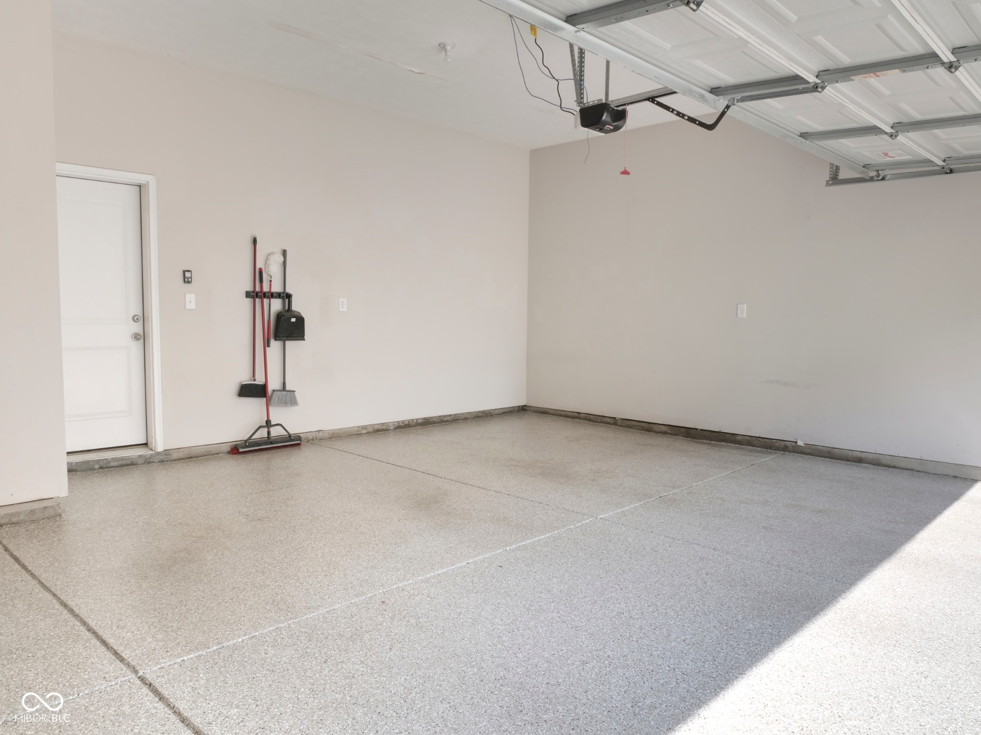 Attached garage with an epoxy-coated floor, painted walls, a white interior door, and an automatic garage door opener