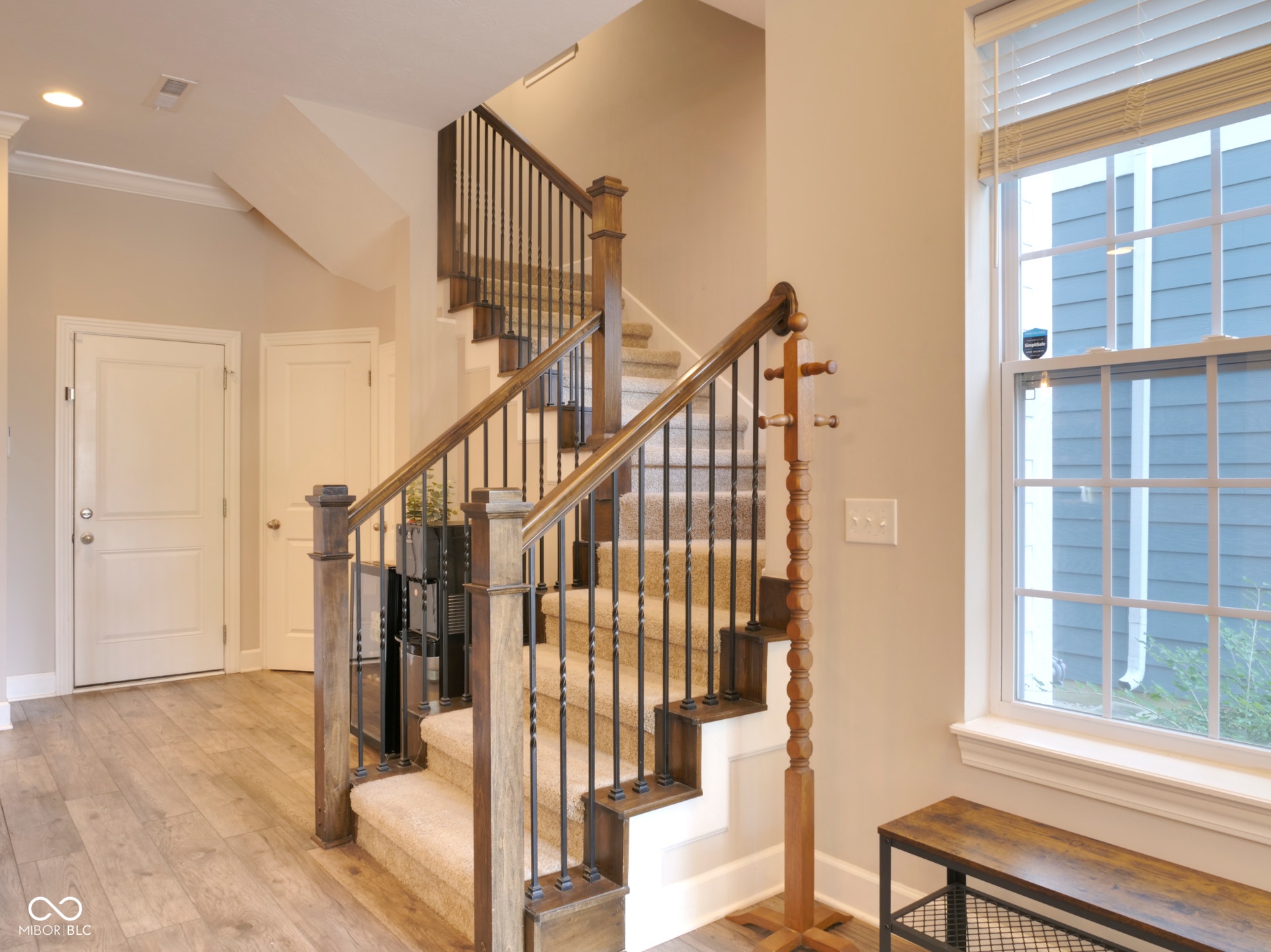 Wood-finish flooring, staircase with carpeted treads, wood and wrought iron balusters, white trim, and a window with blinds