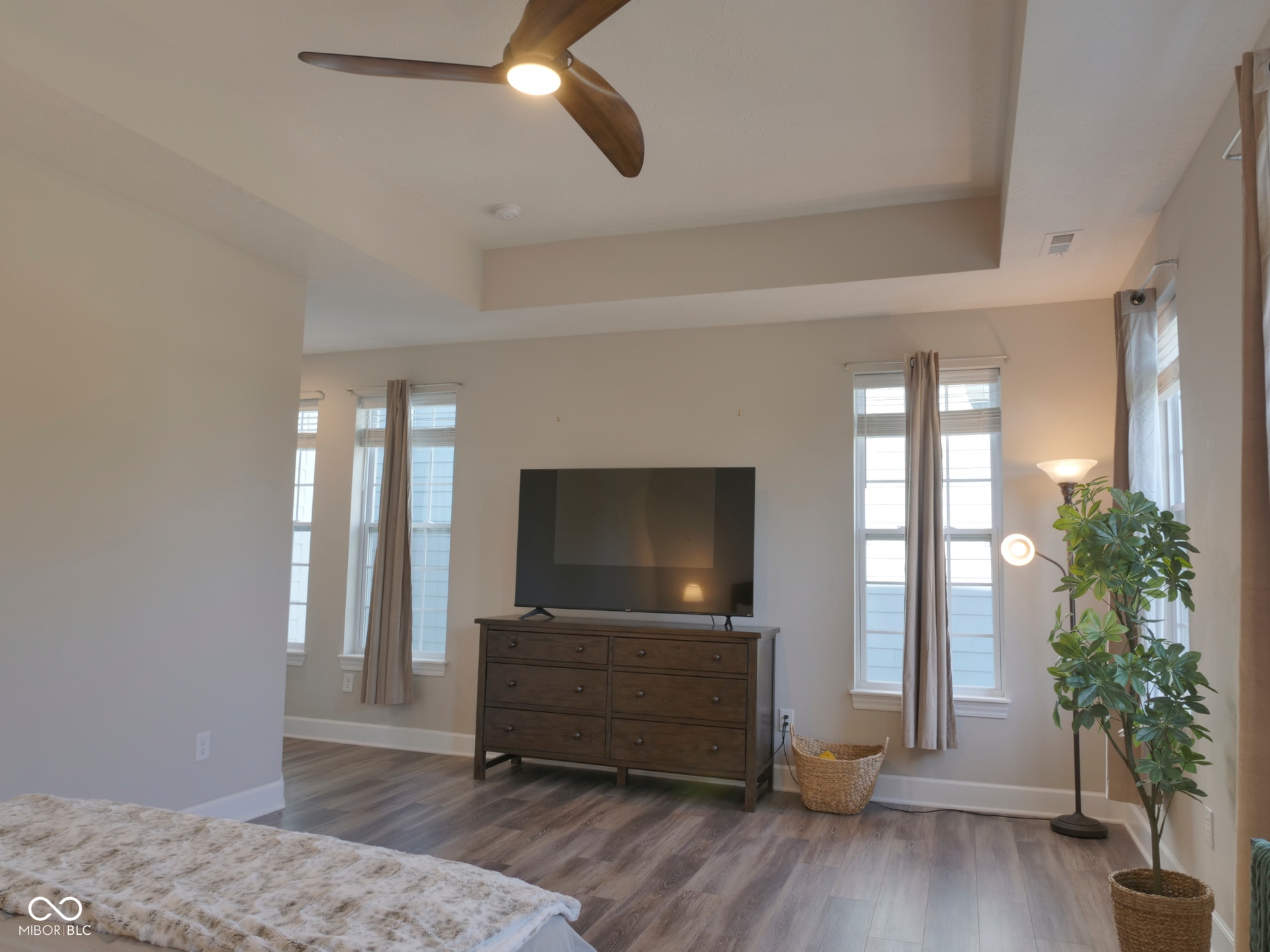 Tray ceiling with a ceiling fan, wood-finish flooring, and multiple windows