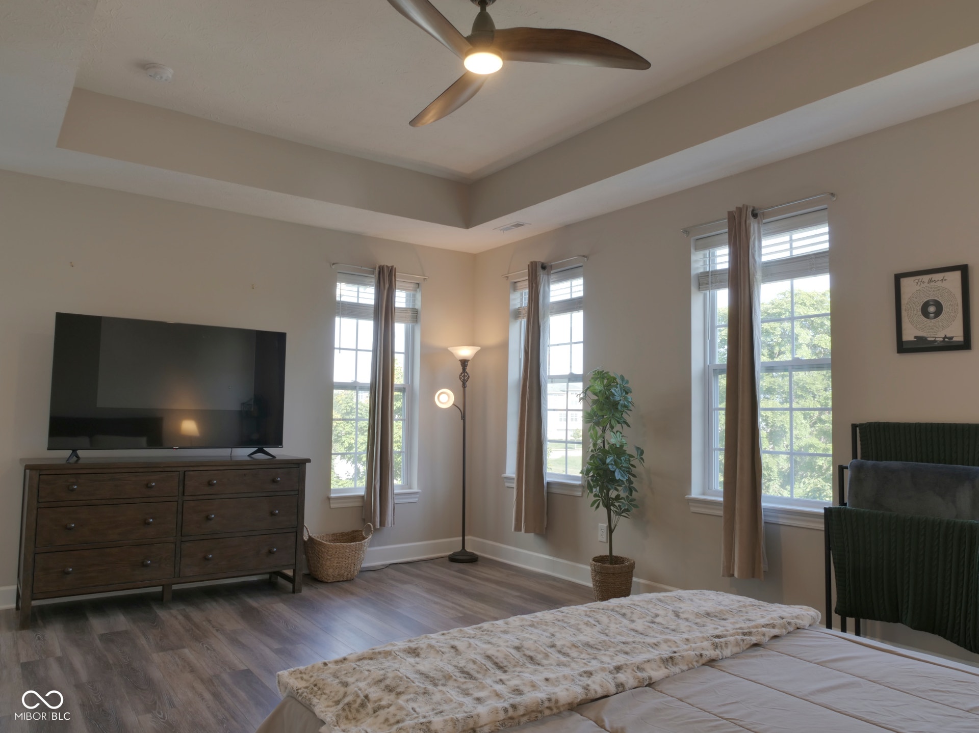 Tray ceiling with recessed lighting, ceiling fan, multiple windows with blinds, and wood-finish flooring