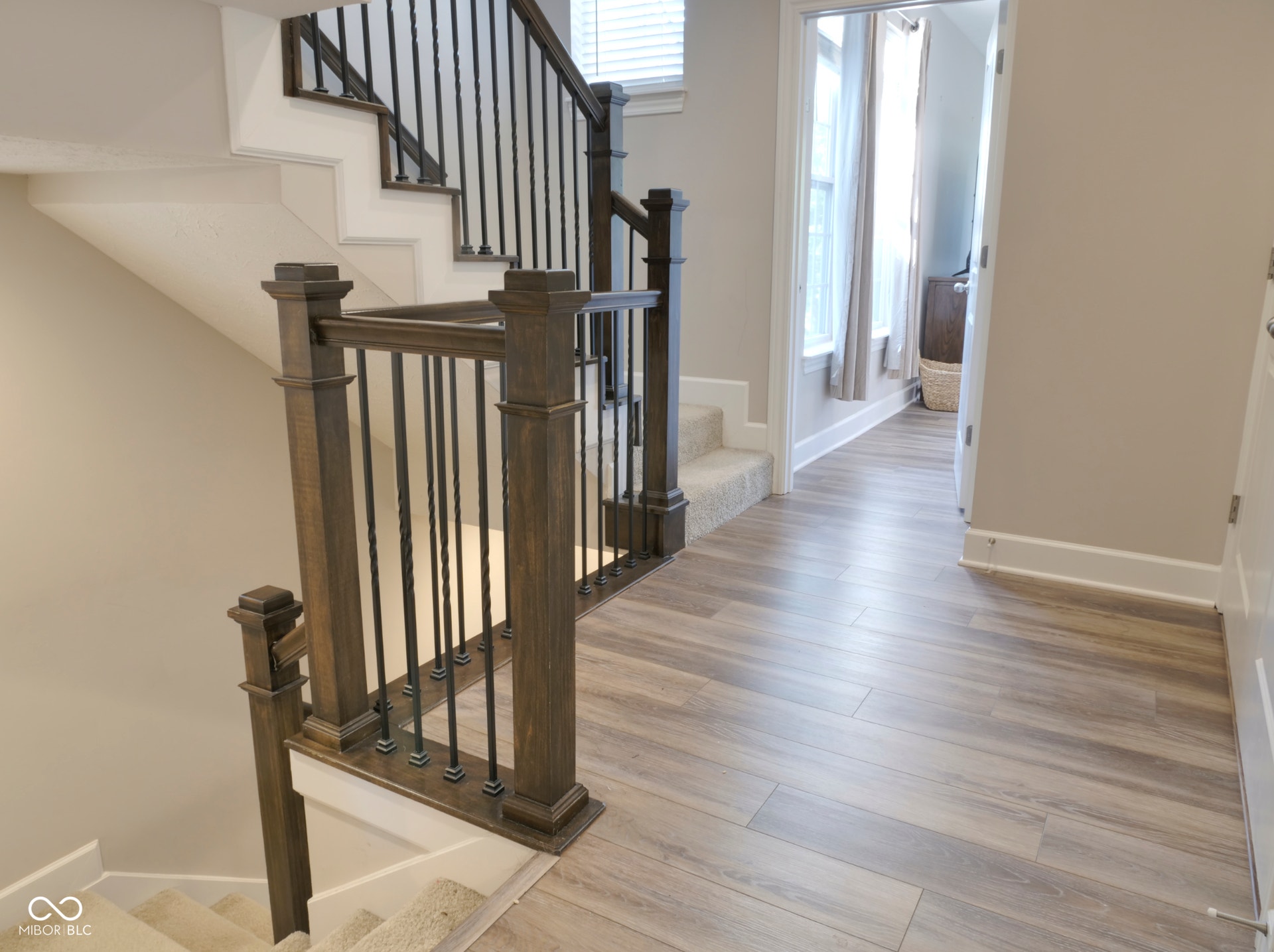 Wood-finish flooring, staircase with dark wood newel posts and metal balusters, and neutral wall paint