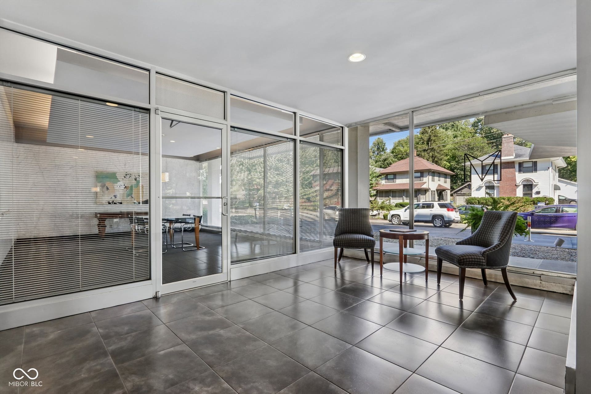 East building: Tile flooring, recessed lighting, expansive window panels, and glass doors with horizontal blinds with access to a conference room