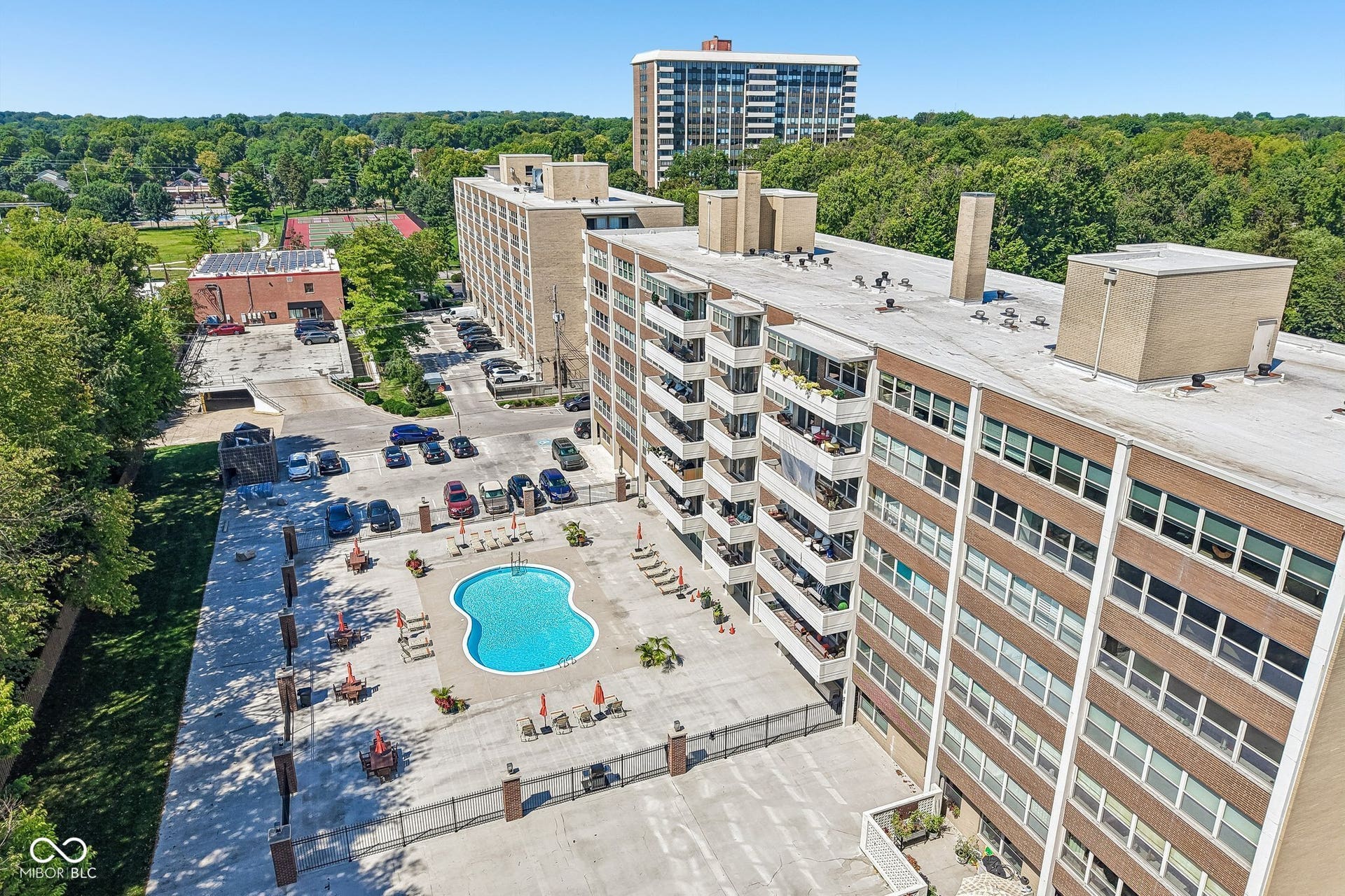 Paved parking area, kidney-shaped swimming pool, surrounding concrete patio, and multi-story building exterior