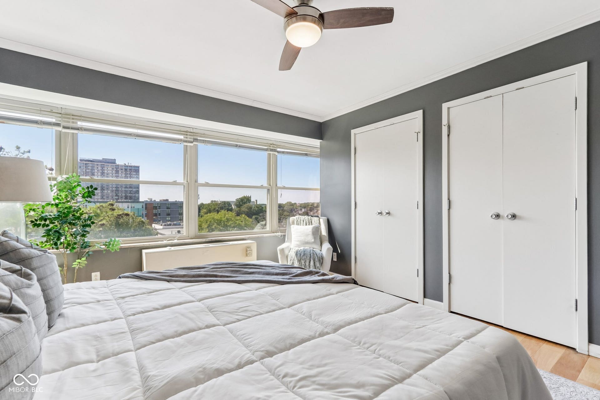 Expansive window wall, wood-finish flooring, two white doors, ceiling fan with integrated lighting, and gray painted walls