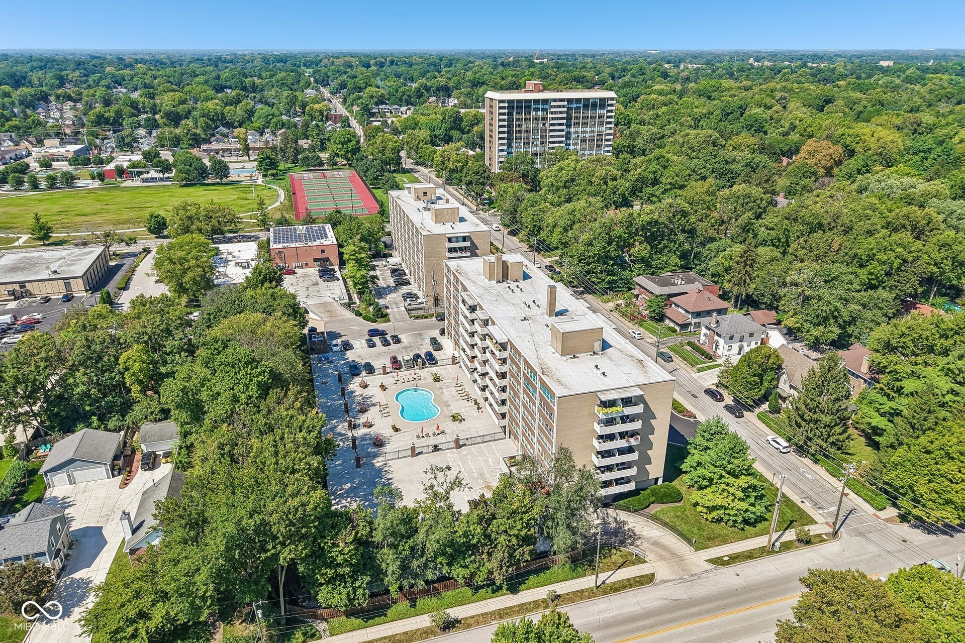 Mid-rise building featuring multiple balconies, a ground-level swimming pool, and dedicated parking areas