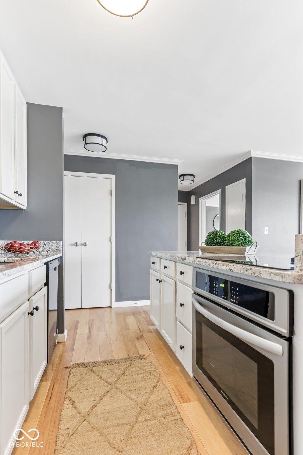 White cabinetry, light wood-finish flooring, stainless steel built-in oven, integrated stovetop, and light-colored countertops
