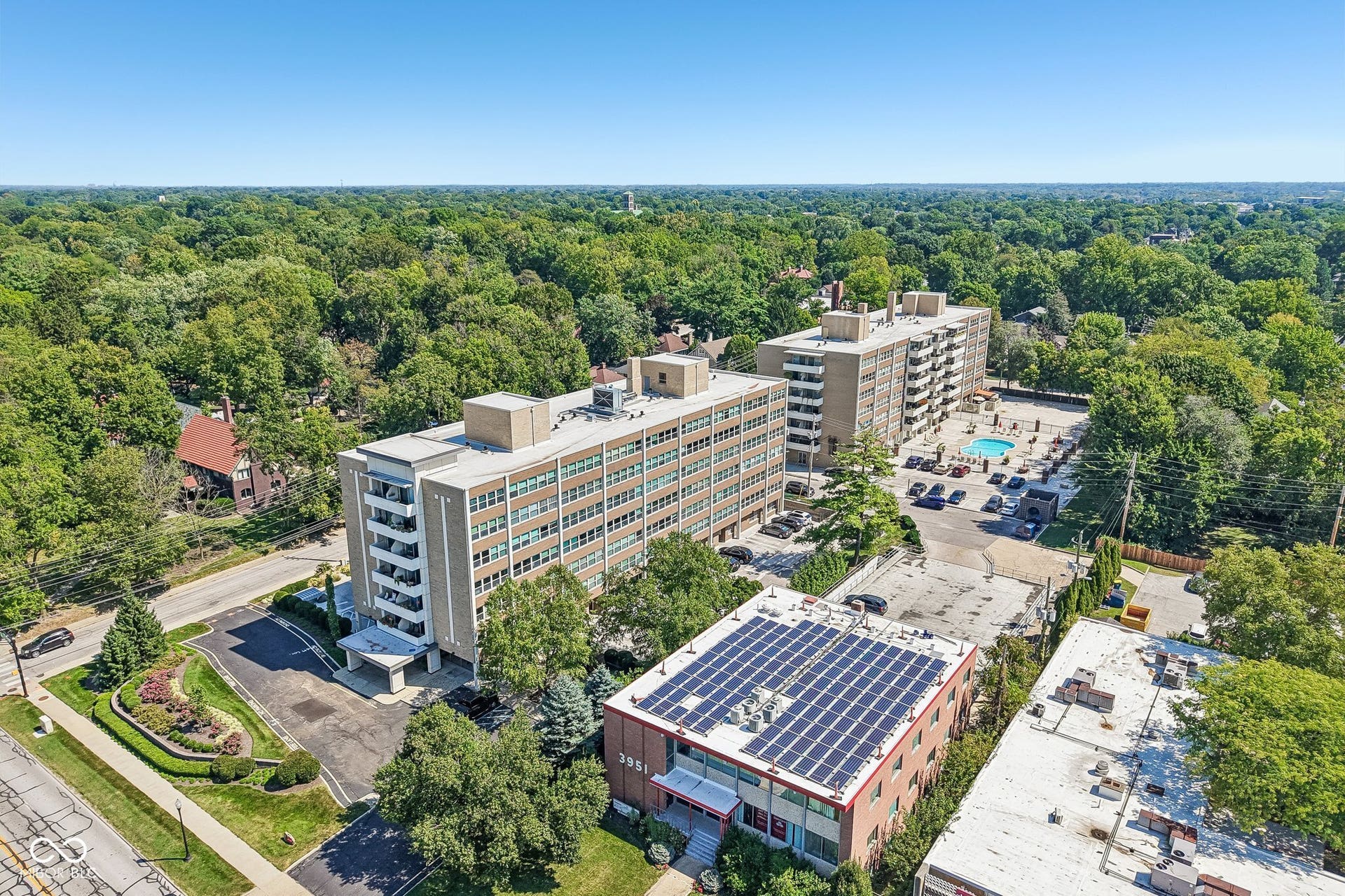 Mid-rise buildings with balconies, mature trees, and a ground-level swimming pool