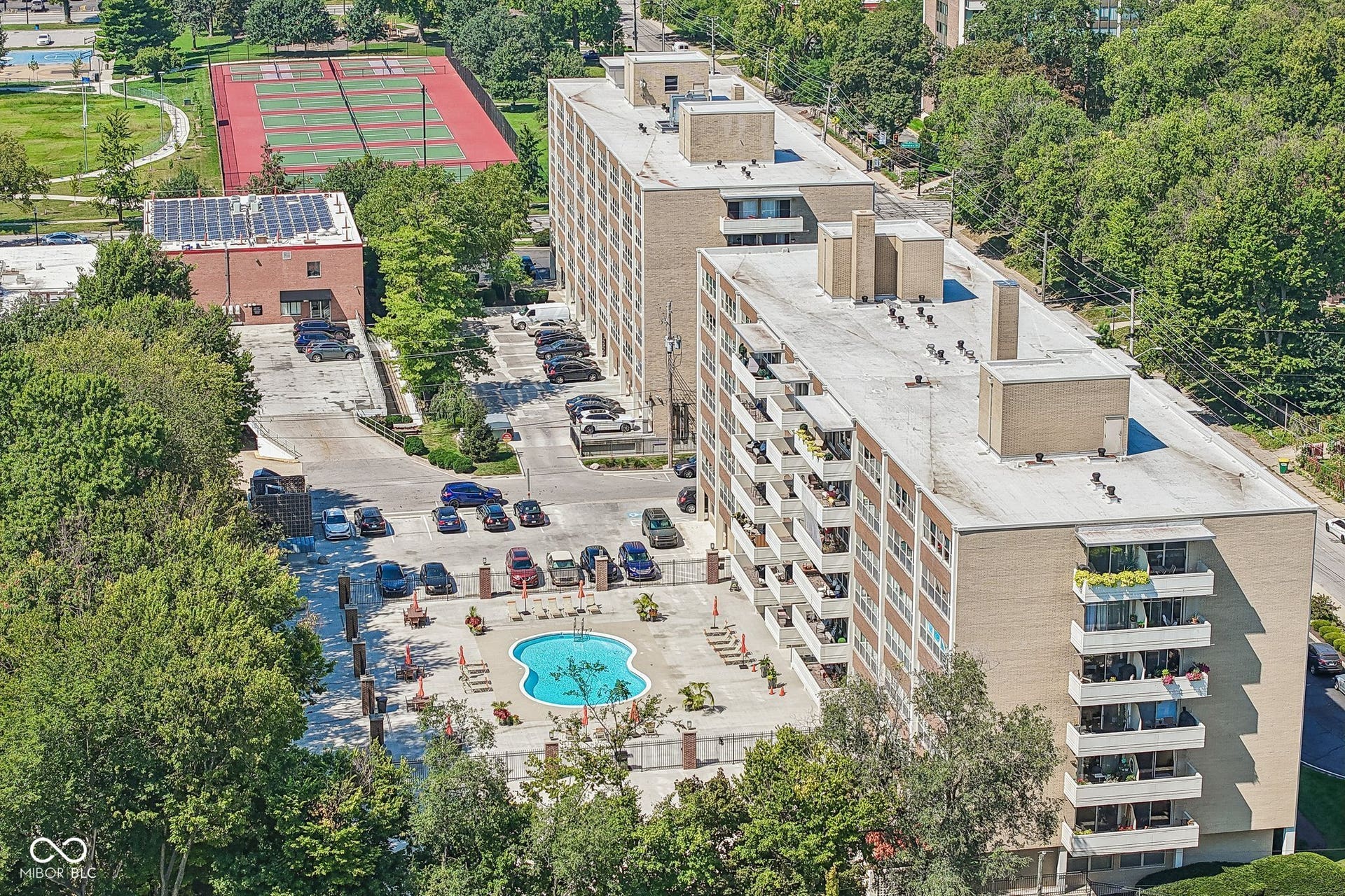 Mid-rise building featuring multiple balconies, a swimming pool, and an adjacent parking area